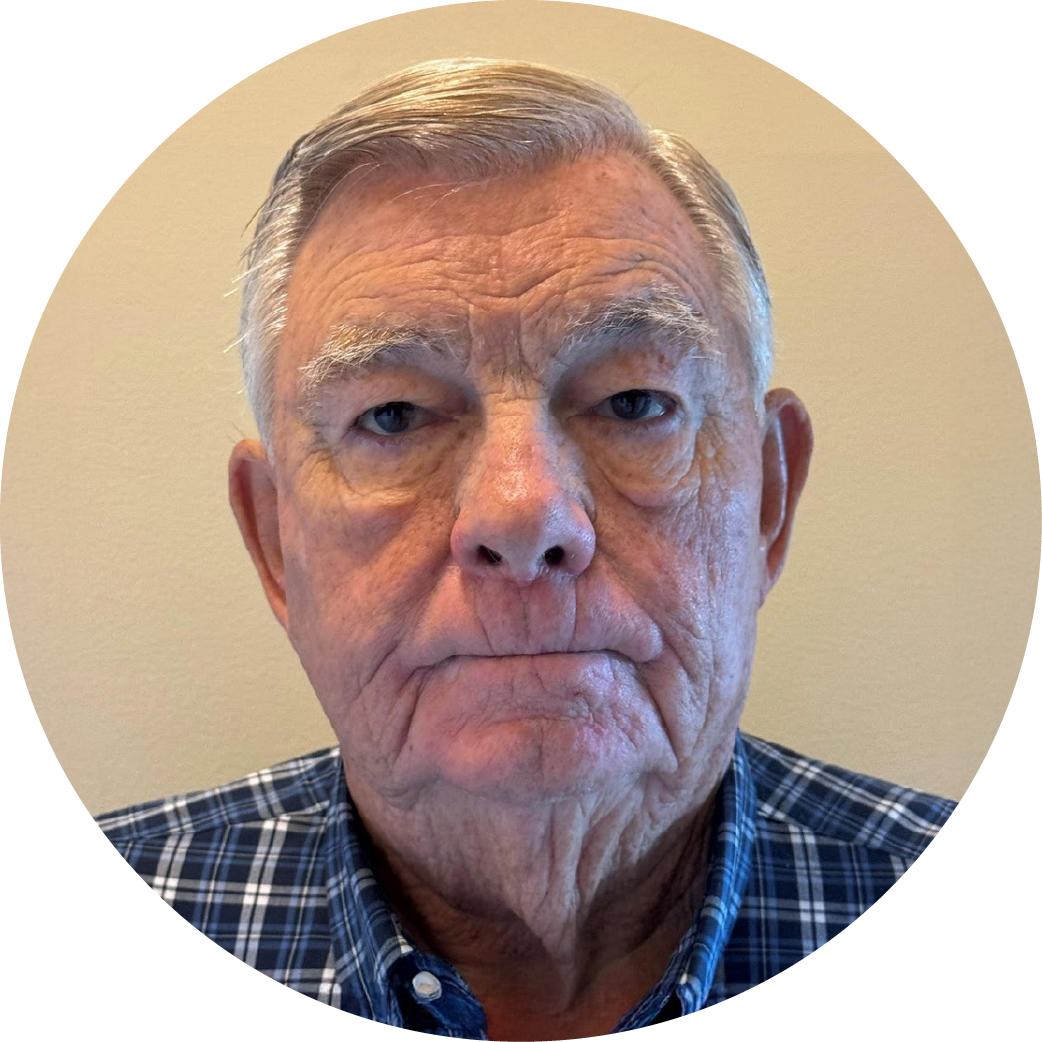 Close-up of an elderly man with gray hair, wearing a blue plaid shirt, against a neutral background.