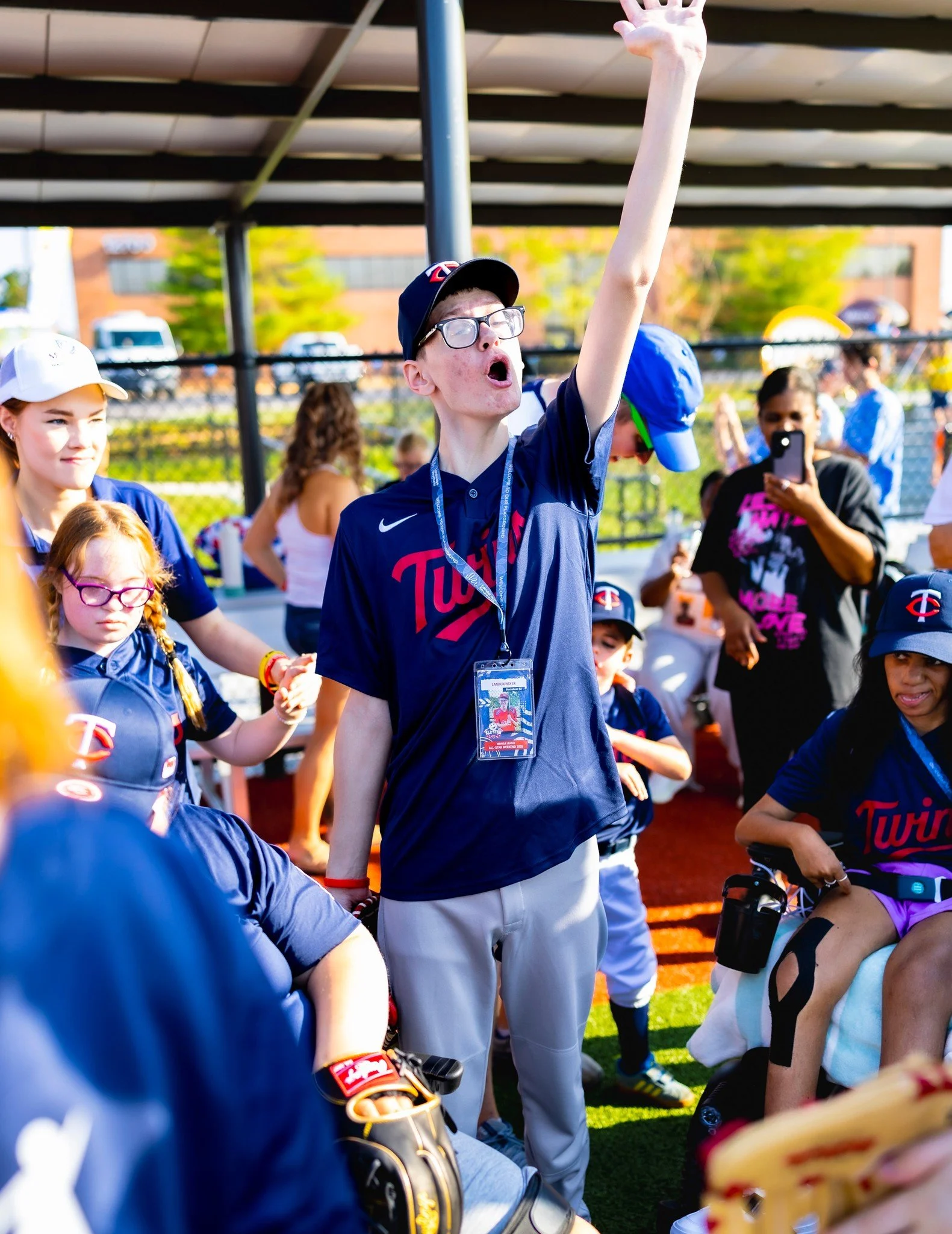 A young man raising his hand and shouting at a baseball game, surrounded by other fans and children wearing Minnesota Twins jerseys, at a baseball stadium.