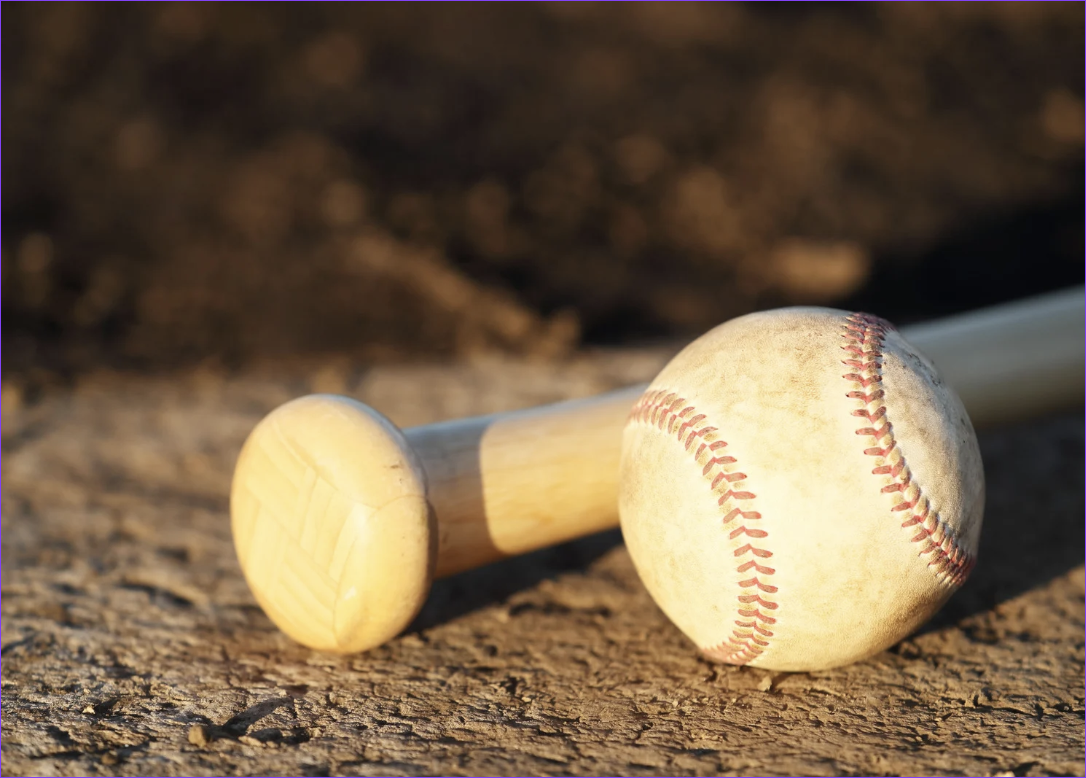 Baseball lying on a dirt field with a wooden bat next to it.