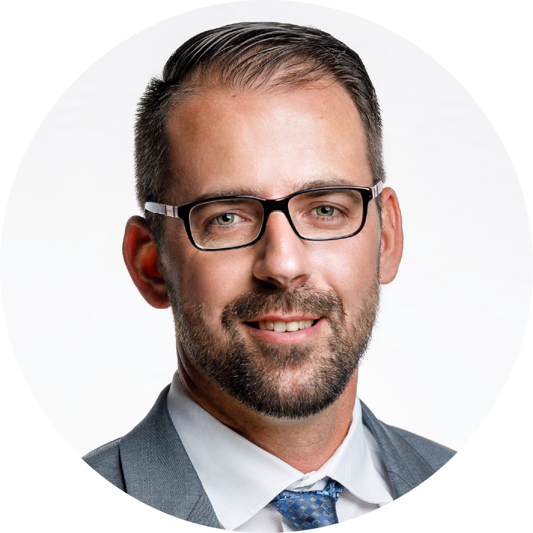 Headshot of a man with glasses, dark hair, a beard, wearing a gray suit and tie, smiling at the camera.