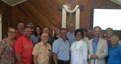 Group of people posing for a photo inside a church with wooden walls and a cross in the background.