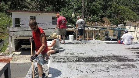 People working on a construction or renovation project outdoors, including shoveling and working on a garage or building.
