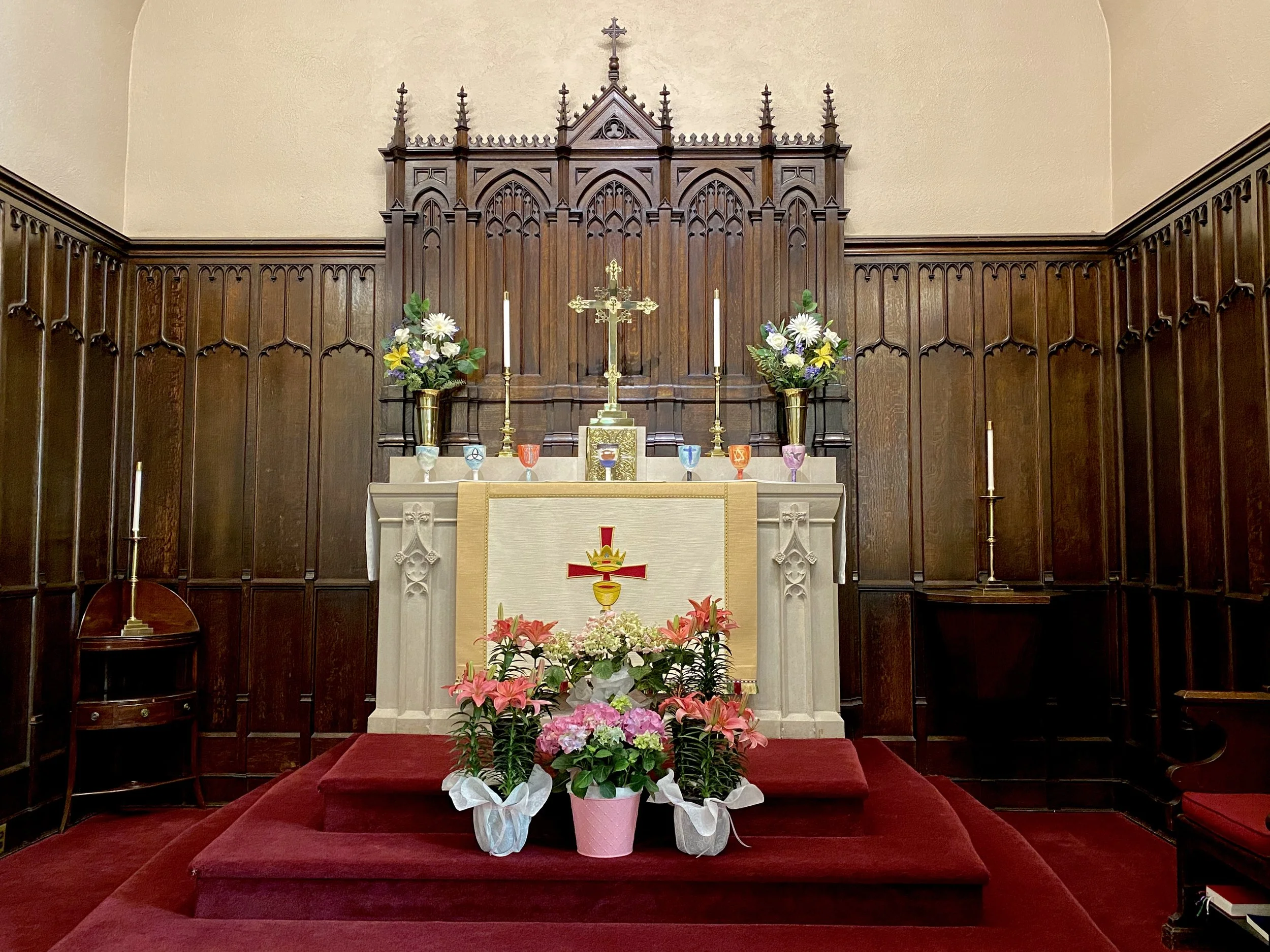 A church altar decorated with flowers, candles, and religious symbols, with a wood-paneled backdrop.