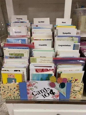 A display of greeting cards in a cardboard tray with labels like 'Get Well,' 'Sympathy,' 'Friendship,' and 'Congratulations'.