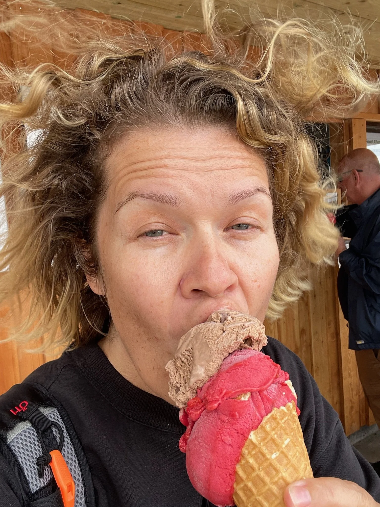 A woman with curly blonde hair enjoying ice cream with two flavors, chocolate and strawberry, in a waffle cone.
