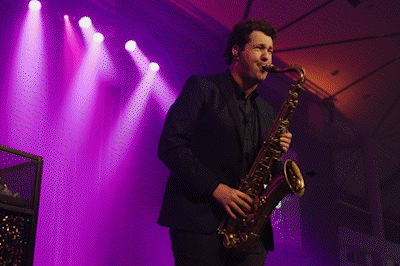 A man playing a saxophone on stage with purple lights.