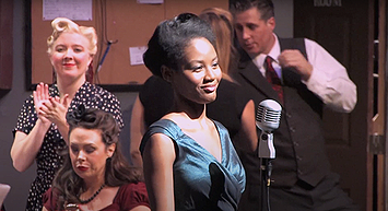 A woman singing at a microphone in a group of people at a social gathering or party