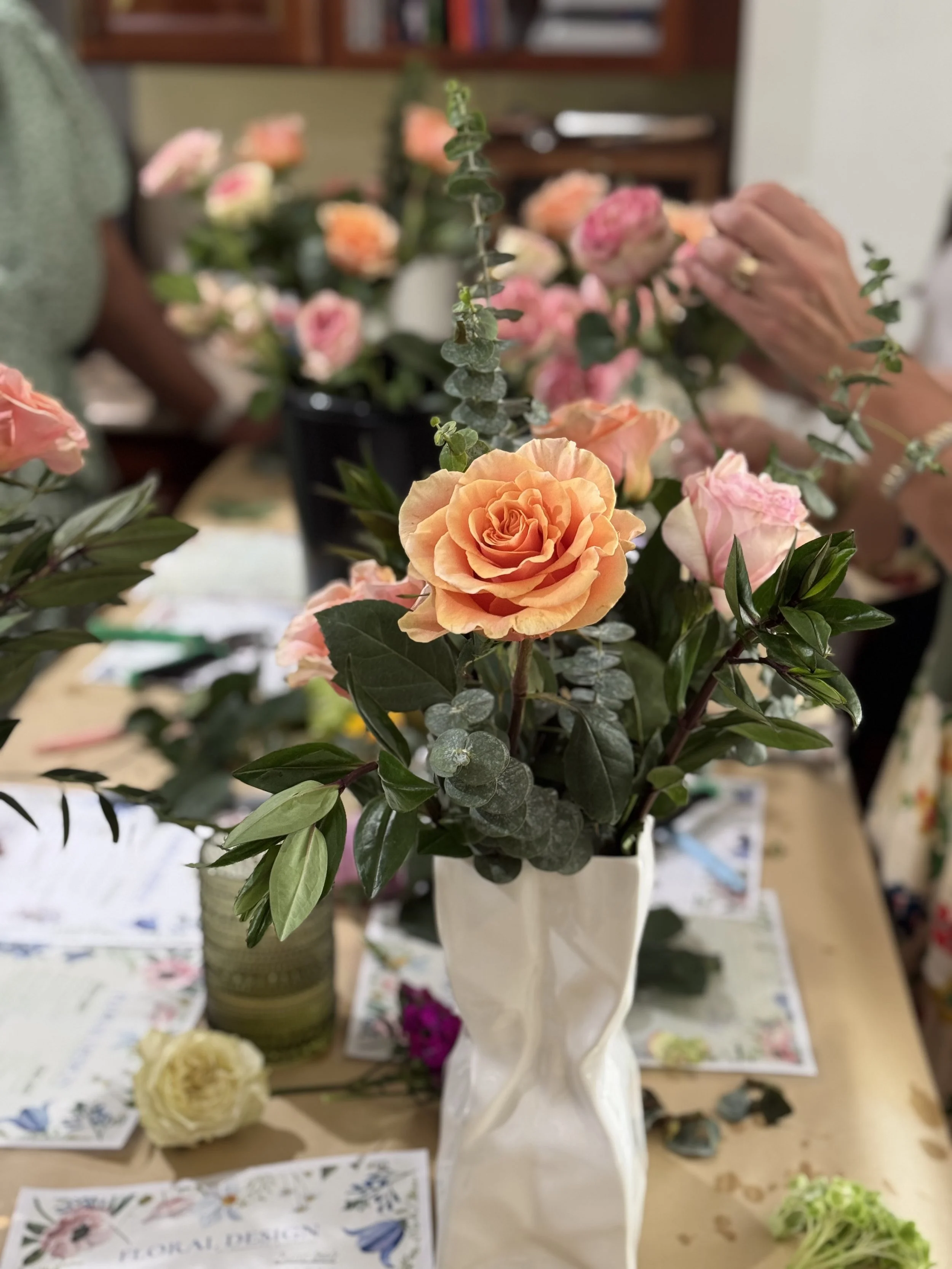 Pink and peach roses in a white ceramic vase on a table.