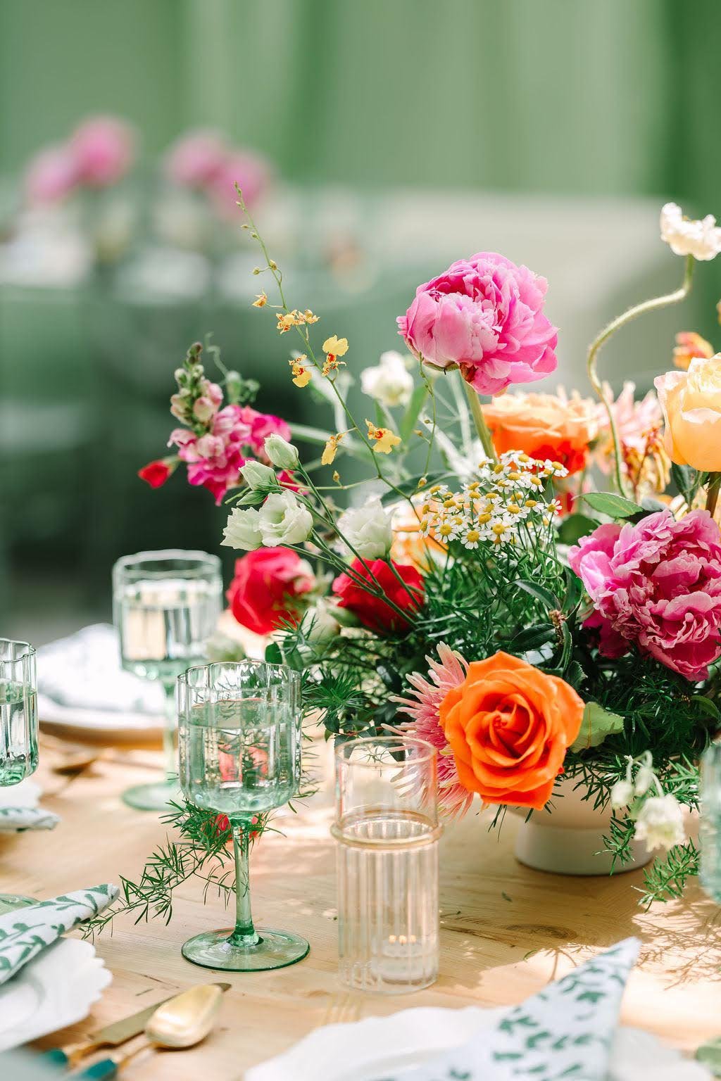 Gilded Event & Floral Design — A floral centerpiece with pink, orange, and white flowers on a dining table with glasses and napkins.
