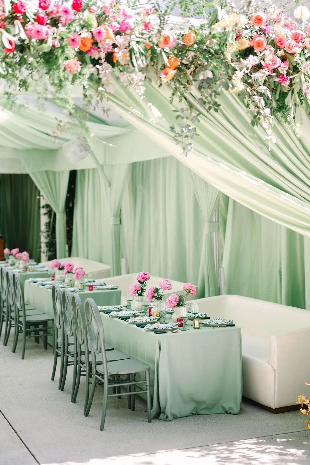 Gilded Event & Floral Design — Decorated event space with green drapes, pink floral centerpieces, and a table set for a gathering.