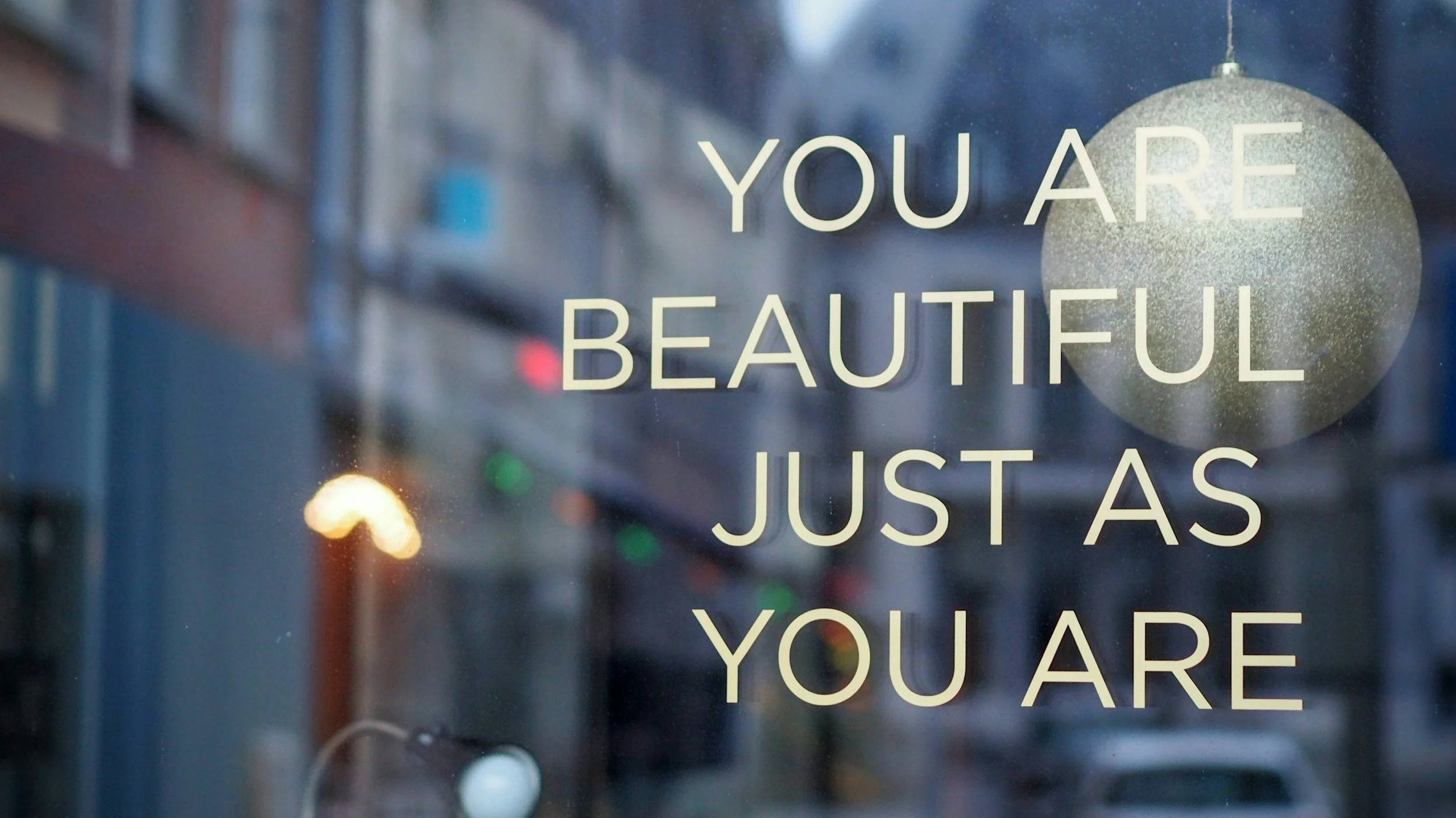 Window with the quote 'You are beautiful just as you are' and a glittery ornament hanging in the background.