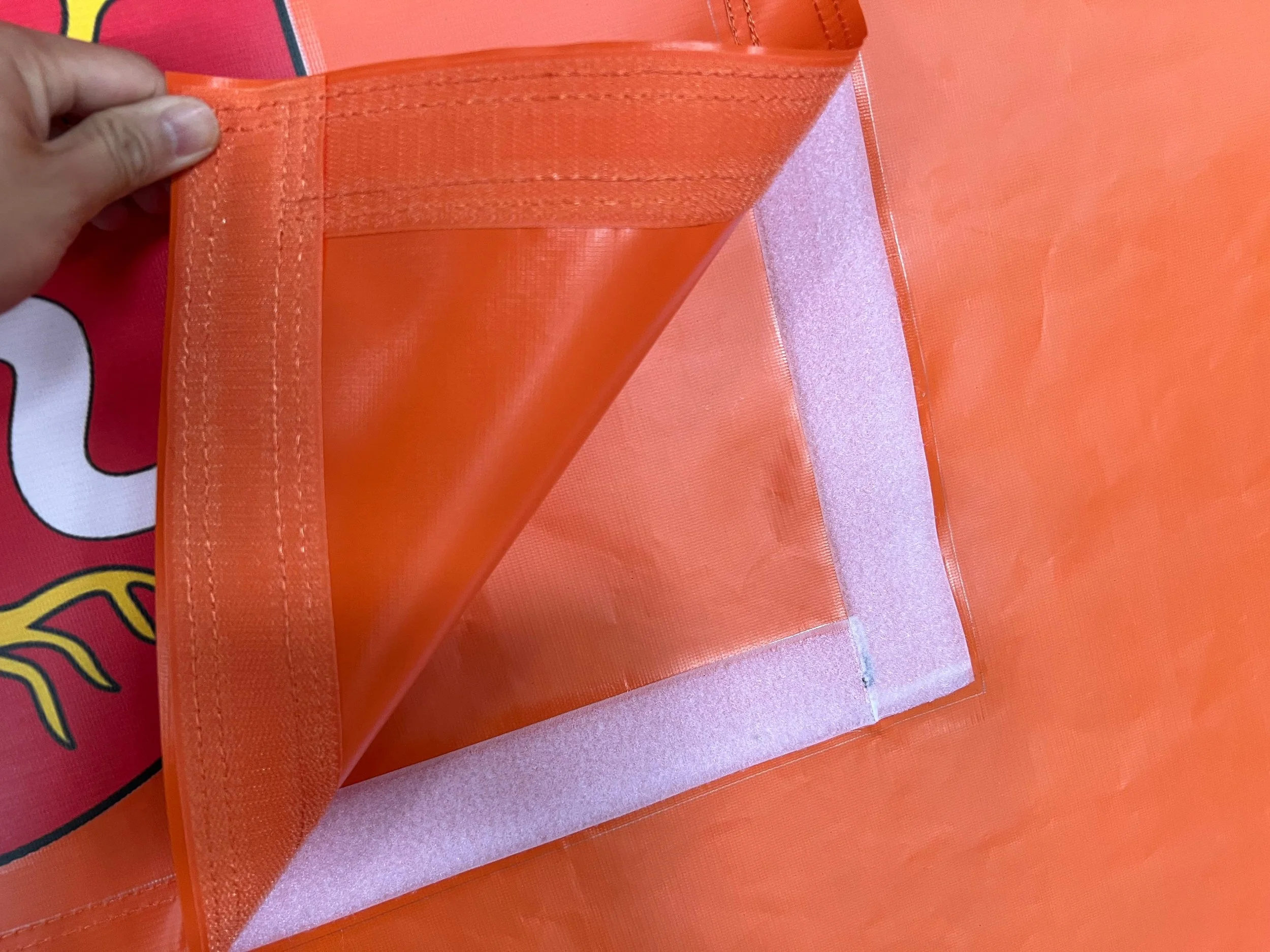 Close-up of orange fabric with a corner unstitched, revealing white interior padding, held by a person's hand.