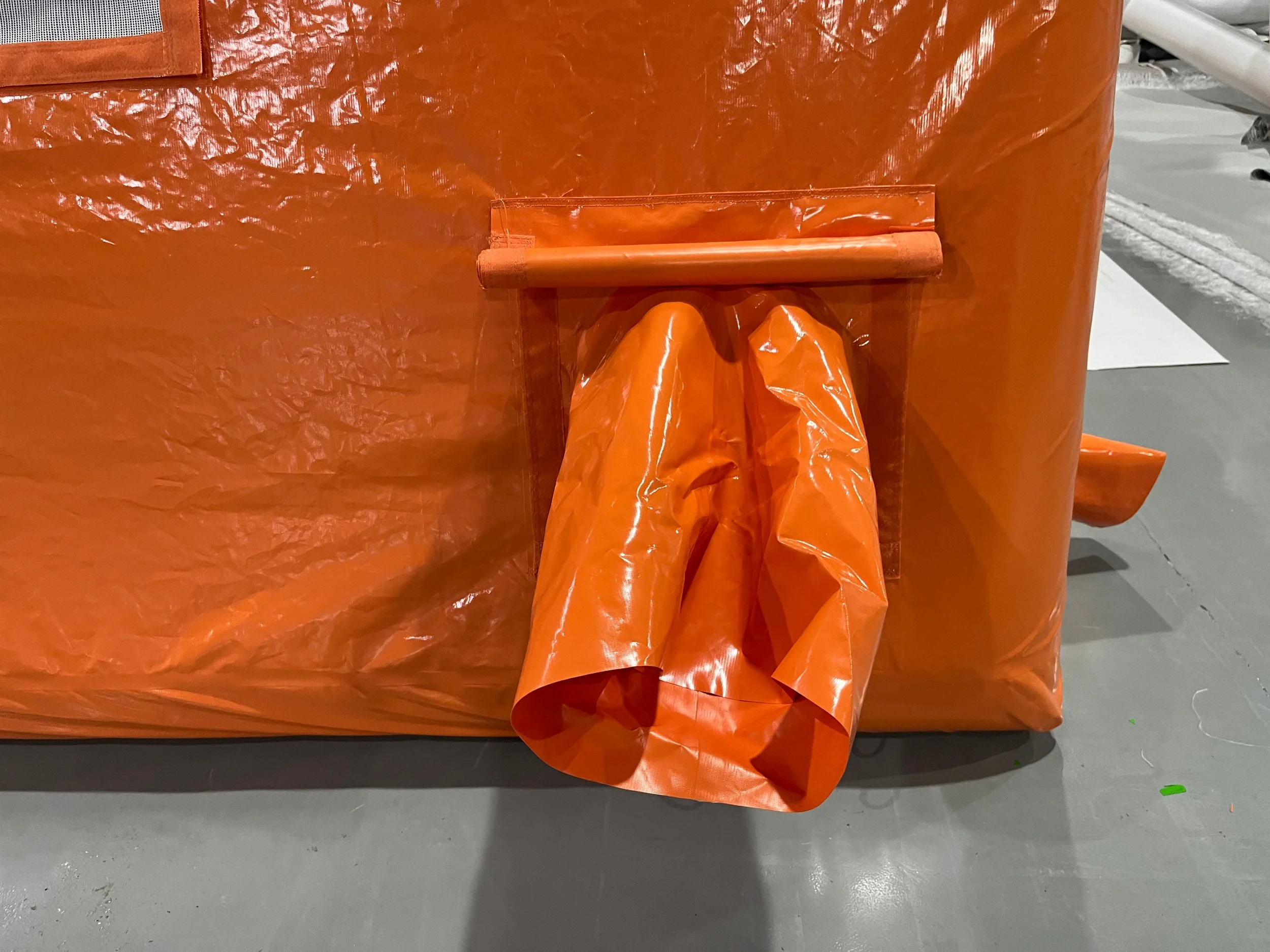 Close-up of a large orange industrial trash bag or tarp secured with a wooden dowel and attached to a larger orange plastic sheet or cover.