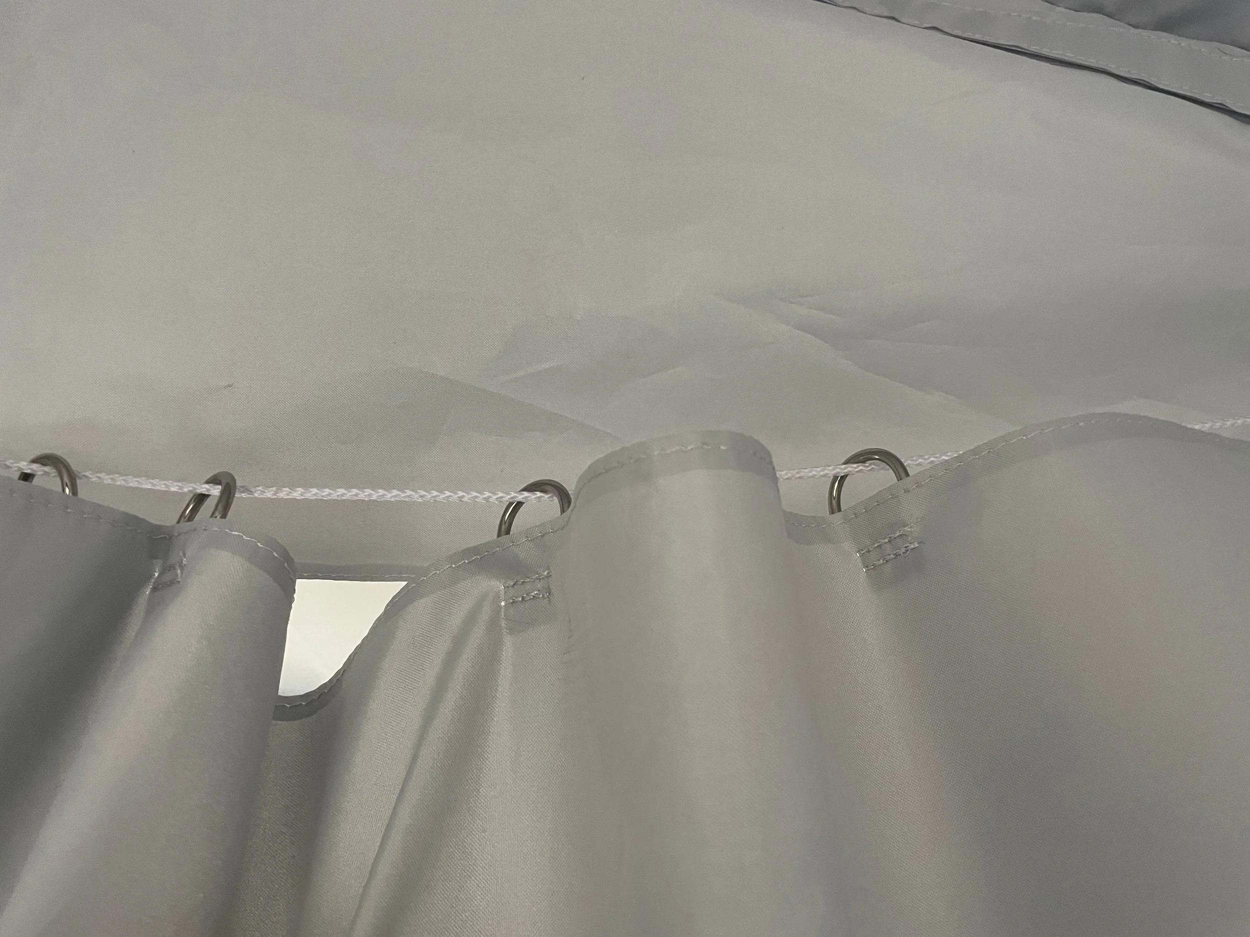 Namiot pneumatyczny Close-up view of a white shower curtain hanging on a rod with metal hooks, showing the top part near the ceiling.