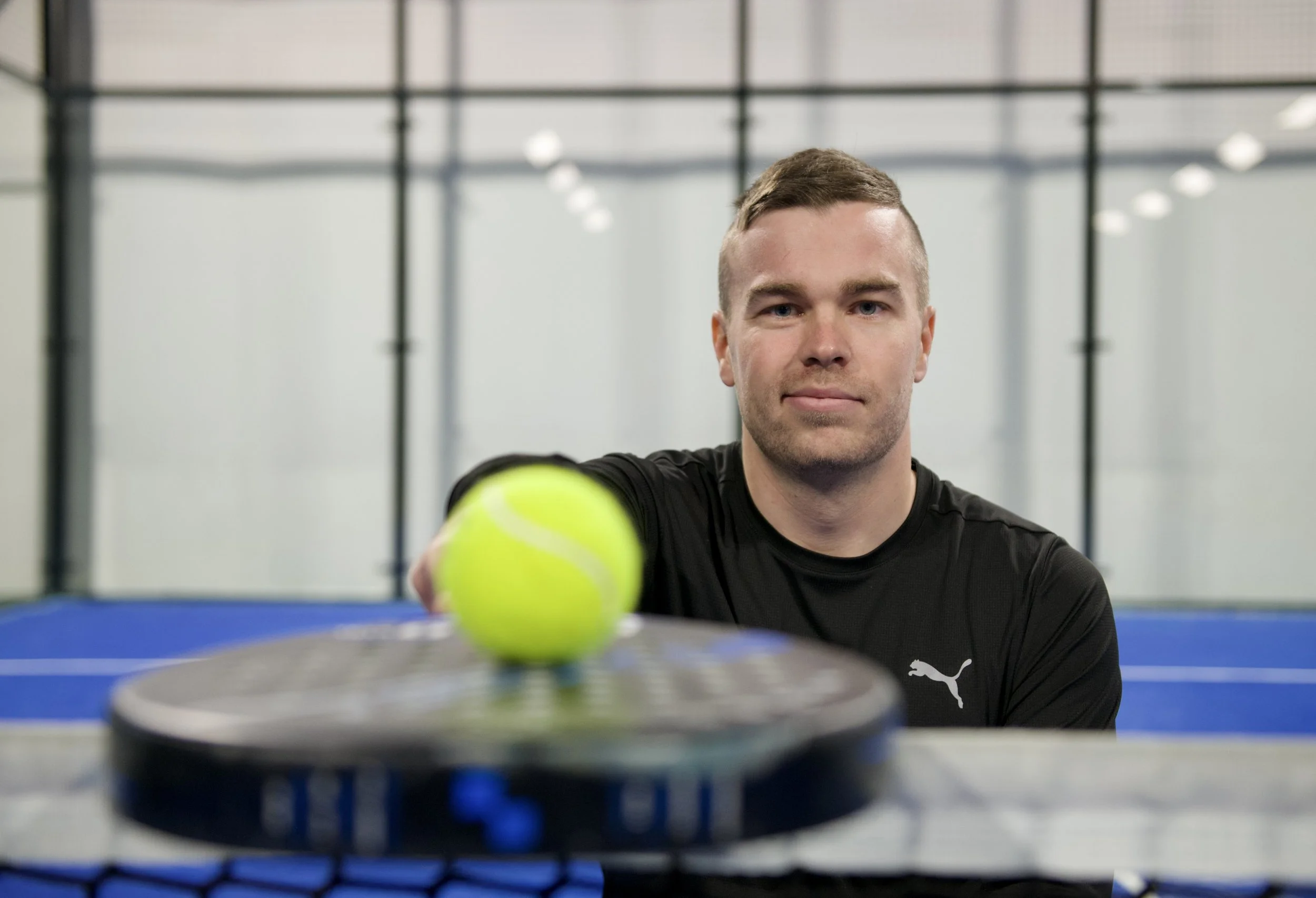 Jere Herrala padelkentällä. Etualalla maila ja pallo.