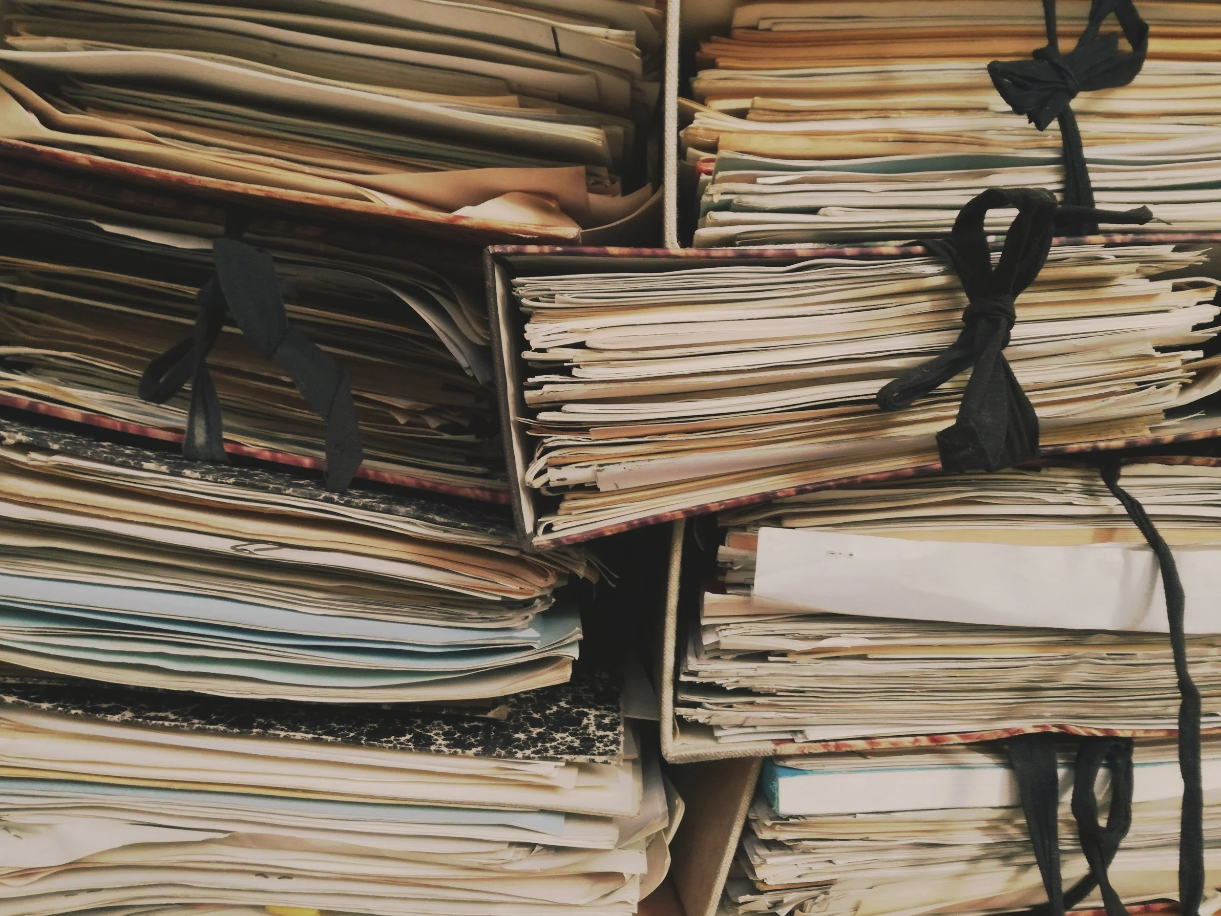 Stacks of disorganized paper files and folders in storage boxes with black ties.