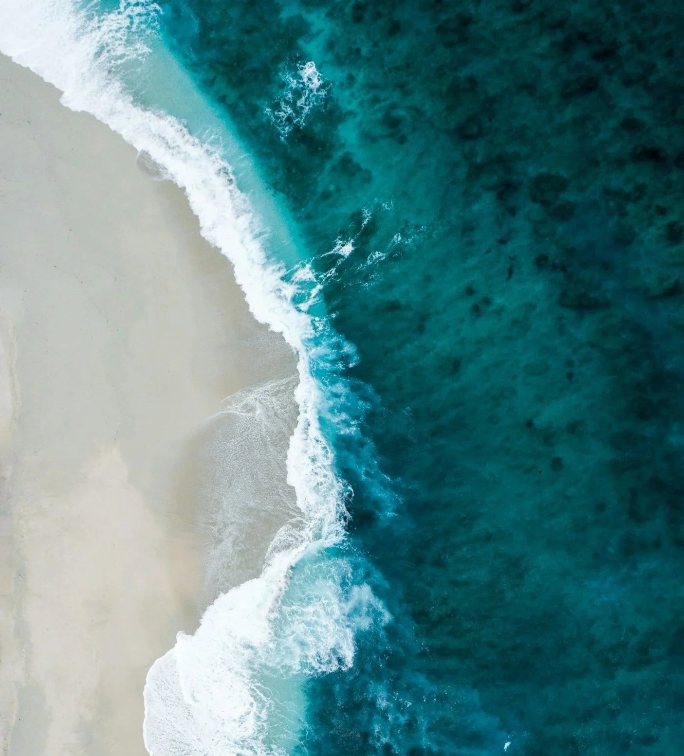 Aerial view of a sandy beach with waves crashing onto the shore in a pattern from left to right