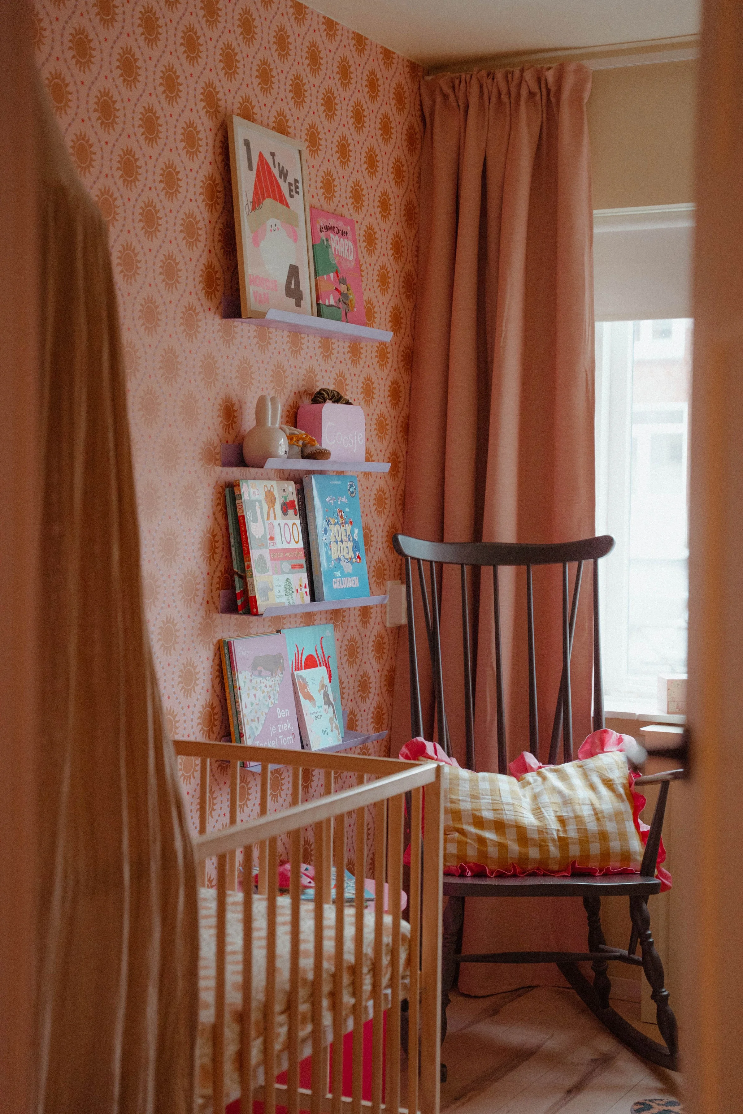 Kleurrijke kinderkamer met zonnetjesbehang van Luz & Moon, houten ledikant en roze accenten.