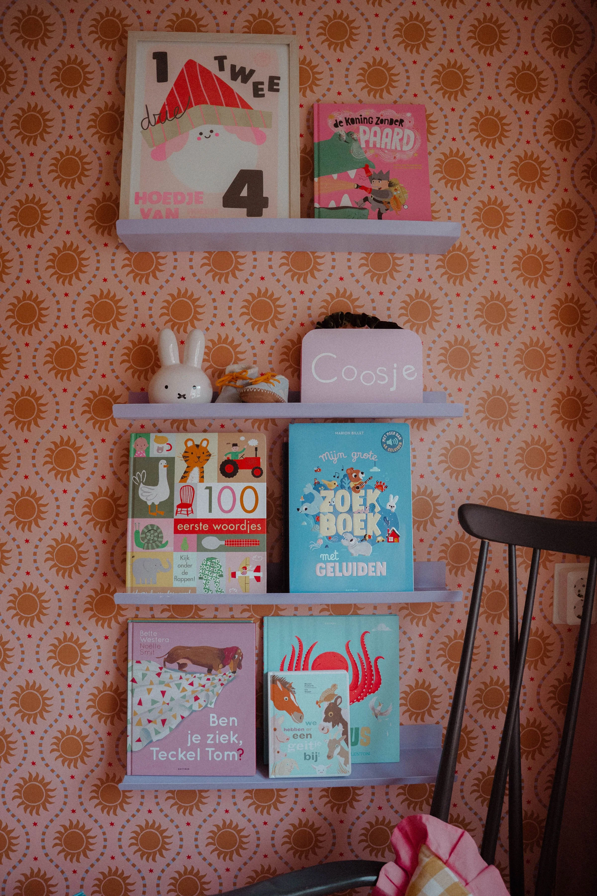 Kleurrijke kinderkamer met zonnetjesbehang van Luz & Moon, houten ledikant en roze accenten.