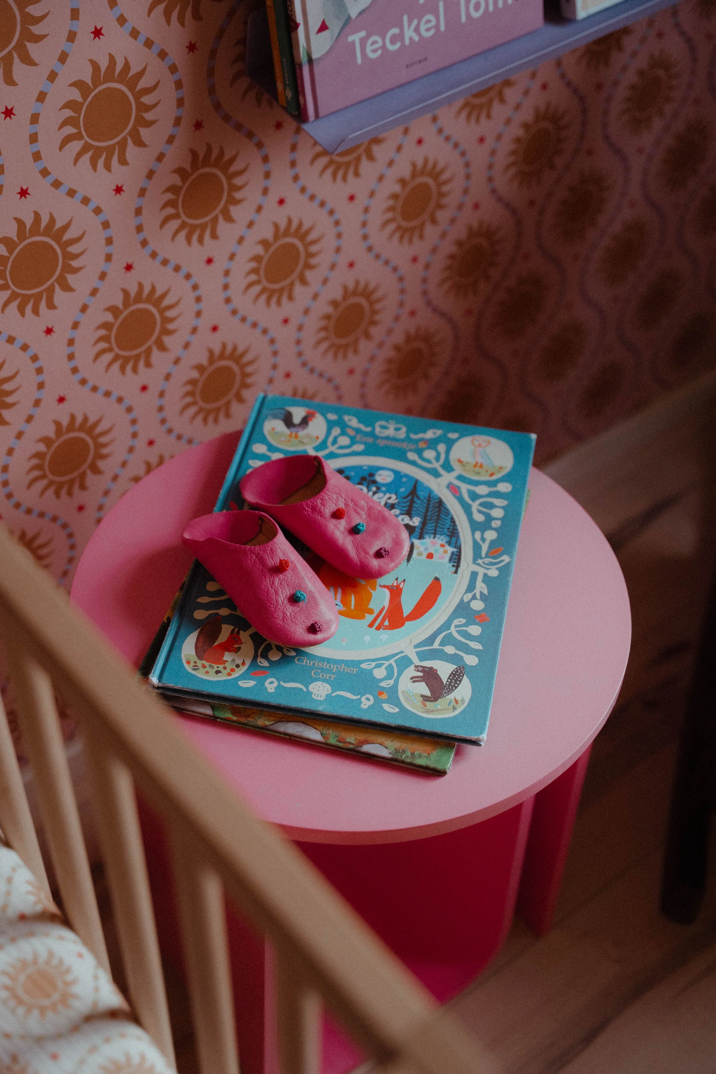 Detailfoto van roze kinderkrukje met kinderboeken en babyslofjes.