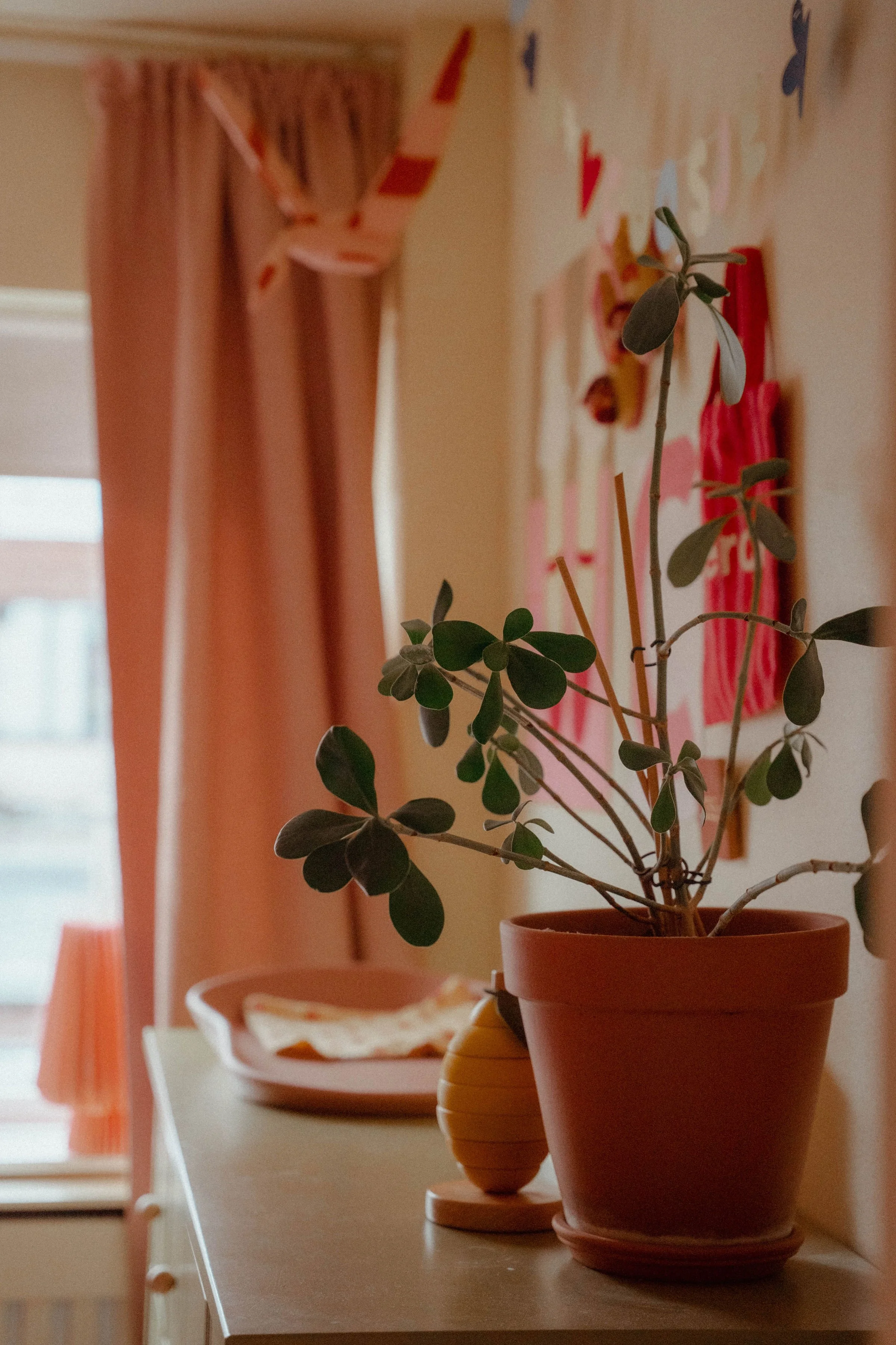 Interieurdetail kleurrijke kinderkamer met groene commode, wanddecoratie, planten en warme gele muur.