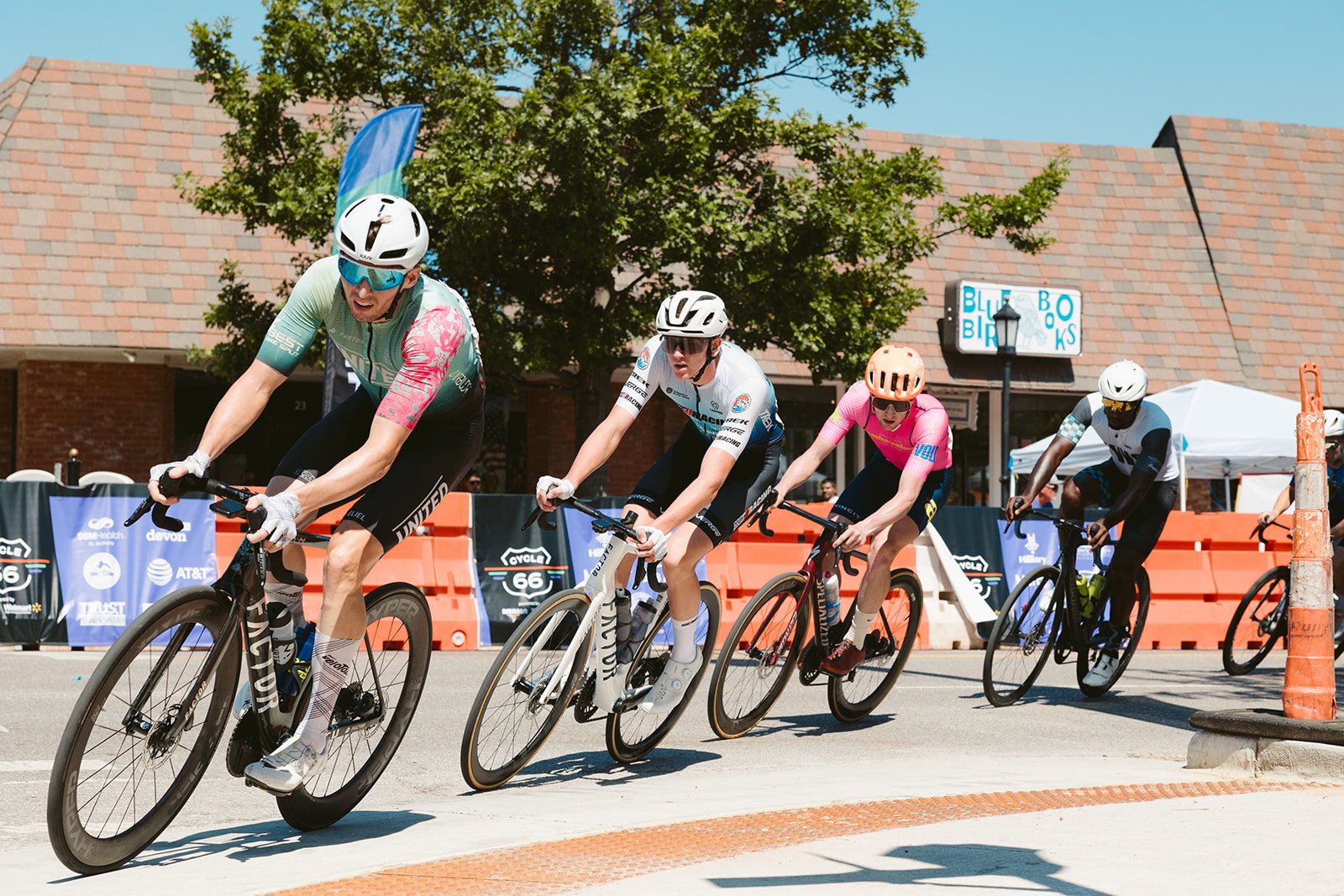Cyclists in a race leaning into a turn on a city street during daytime, wearing helmets and colorful jerseys.