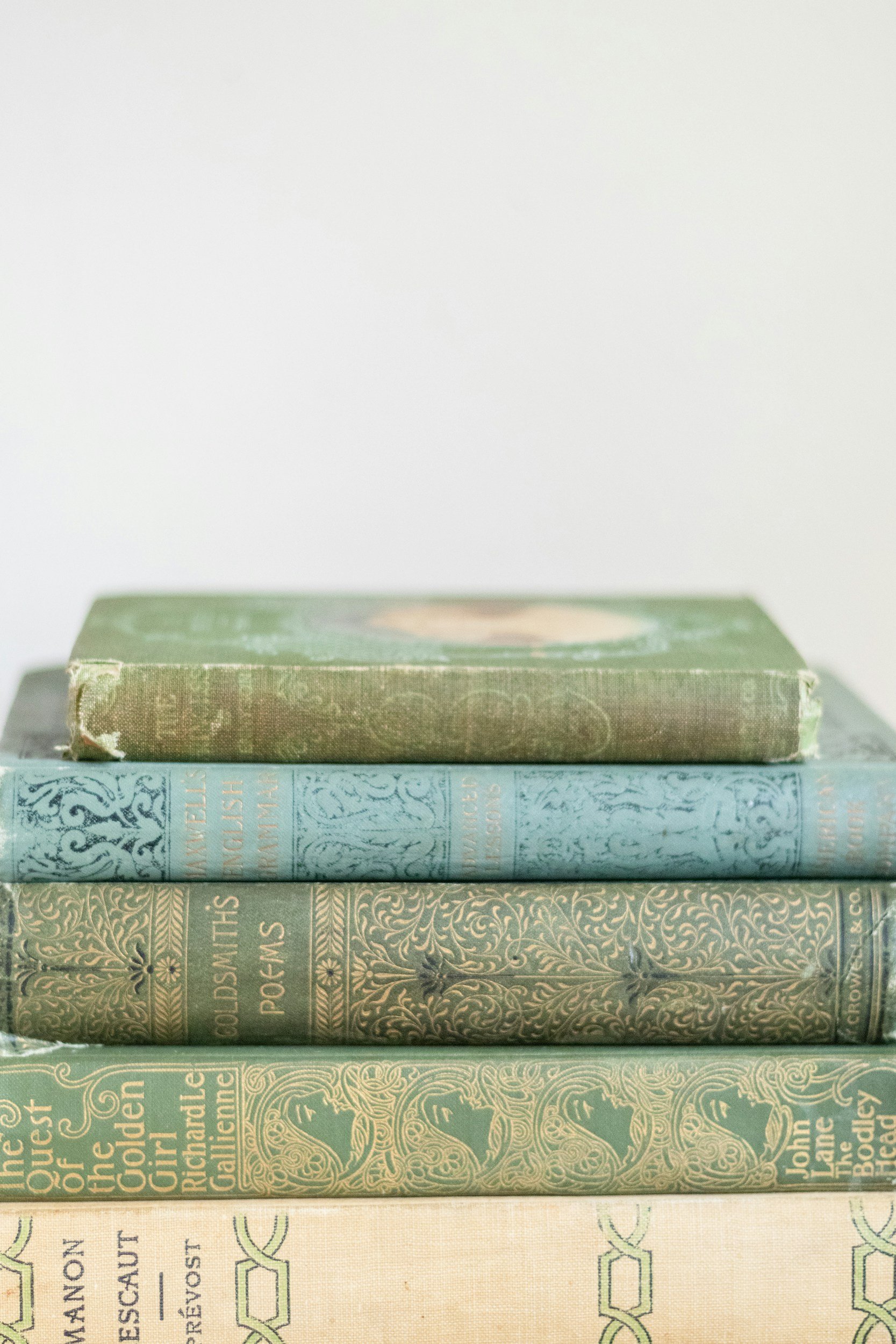 Stack of five vintage books, with the bottom book titled 'The Quest of the Golden Girl' by Richard Callen, the second 'Goldsmith's Poems', and others in between with faded covers.