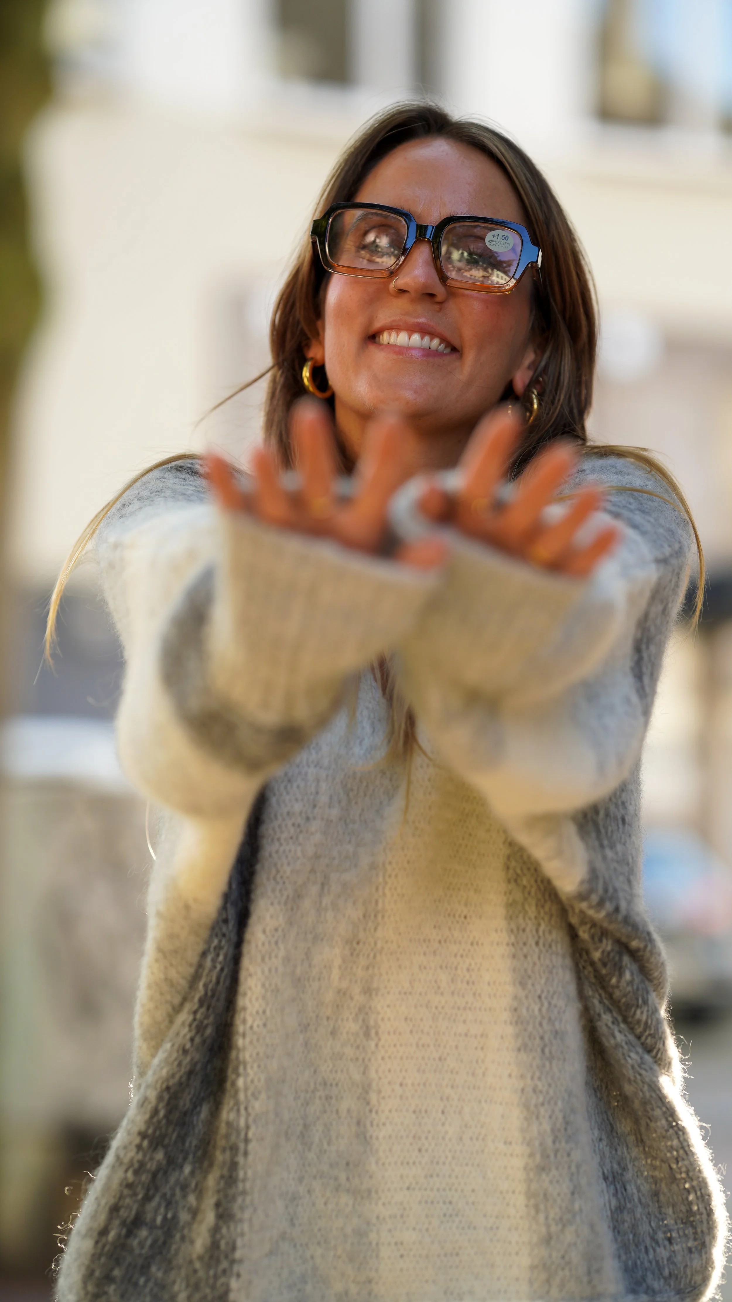 Junge Frau mit Brille, die nach vorne greift und lächelt, im Freien bei Tageslicht