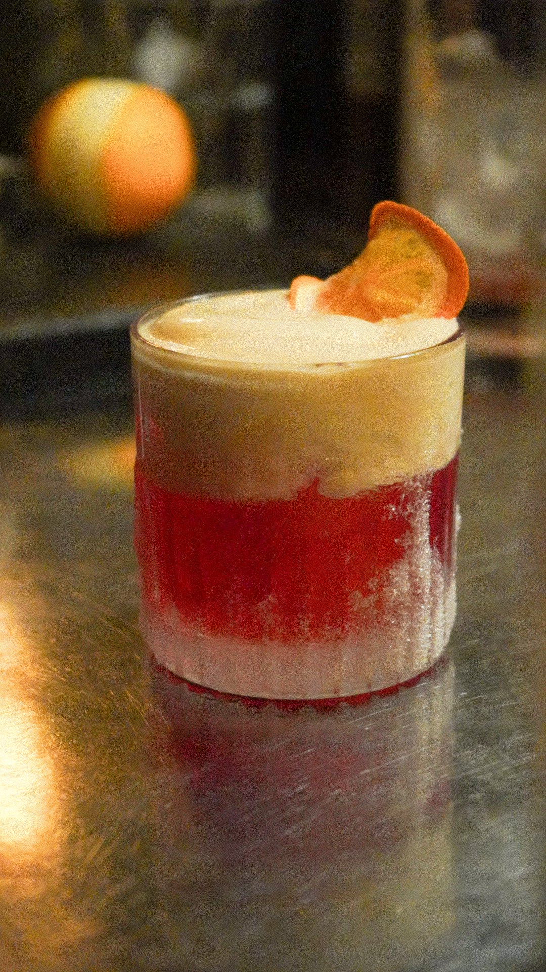 Ein Glas mit Schichtdessert aus rotem Fruchtpüree, Vanillecreme und Garnierung mit einer Orangenscheibe.