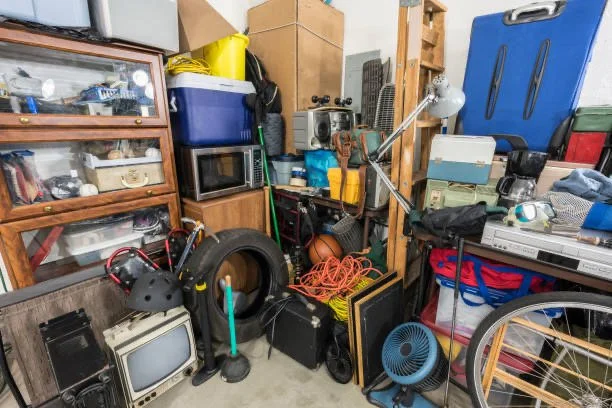 A cluttered garage with various stored items including a microwave, vintage TV, bicycle, a fan, and several boxes and tools.