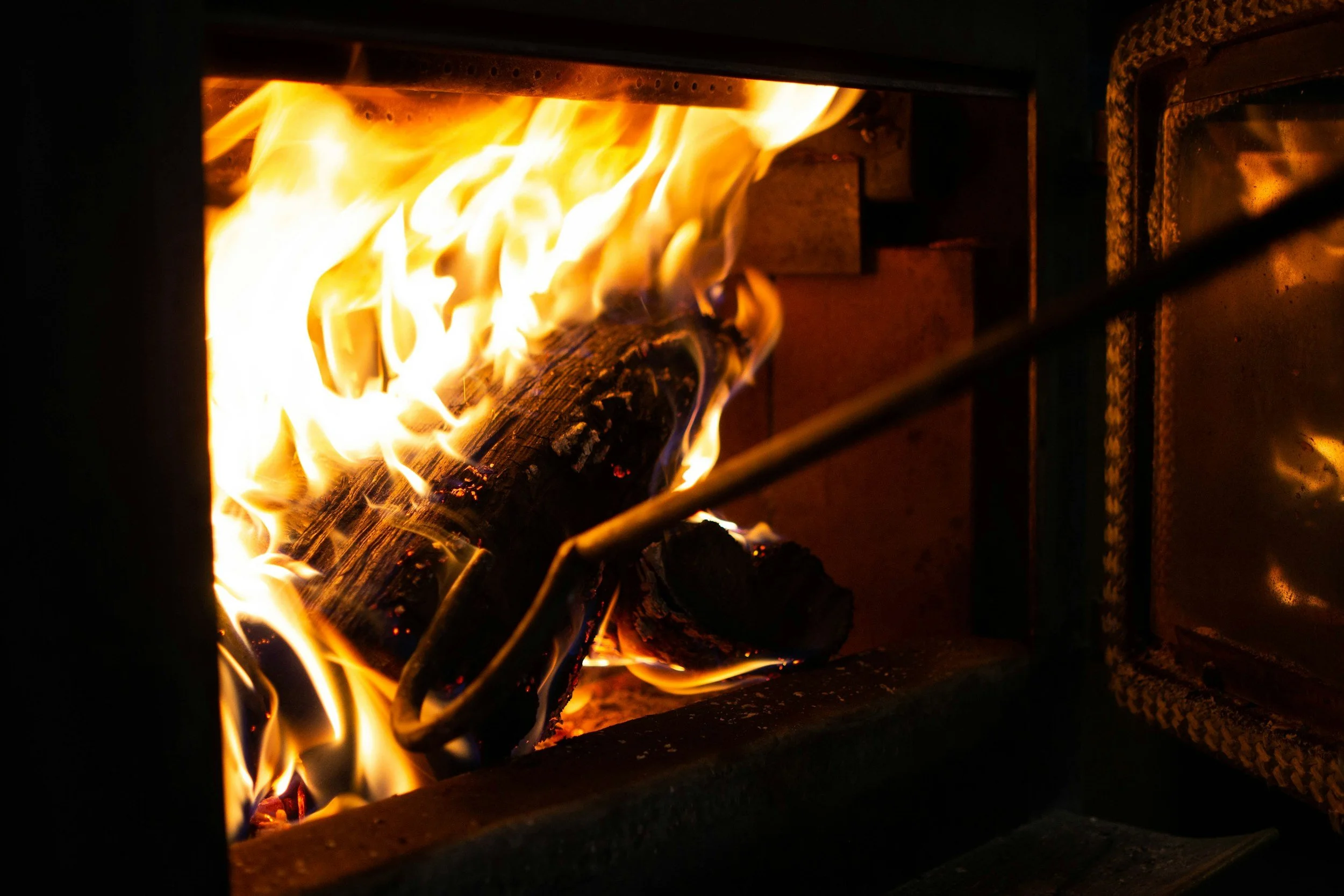 Logs burning inside a metal fireplace with visible flames and embers.