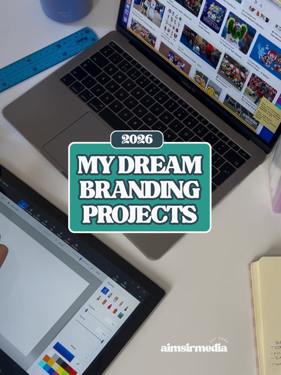 A workspace with a silver laptop displaying a website, a black tablet with design tools, a blue ruler, and a yellow notepad on a white desk. The image has a text overlay reading '2026 MY DREAM BRANDING PROJECTS' and a small logo 'aimsirmedia' at the bottom.