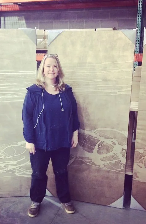 A woman with blonde hair standing in front of large wooden boards in a warehouse.