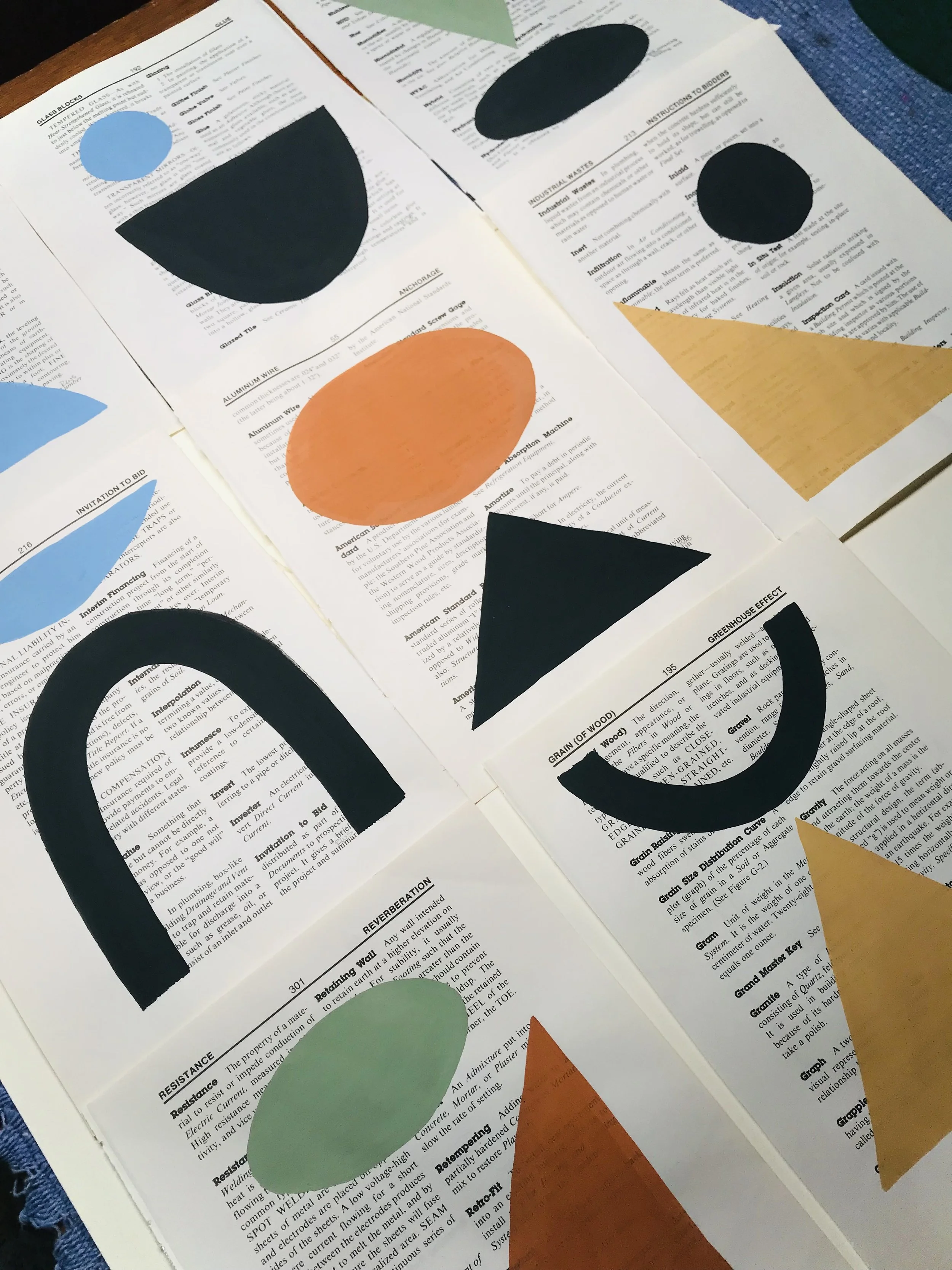 Open book pages decorated with abstract shapes of various colors, including black semicircles, a black triangle, a green oval, an orange circle, and orange and yellow triangles.
