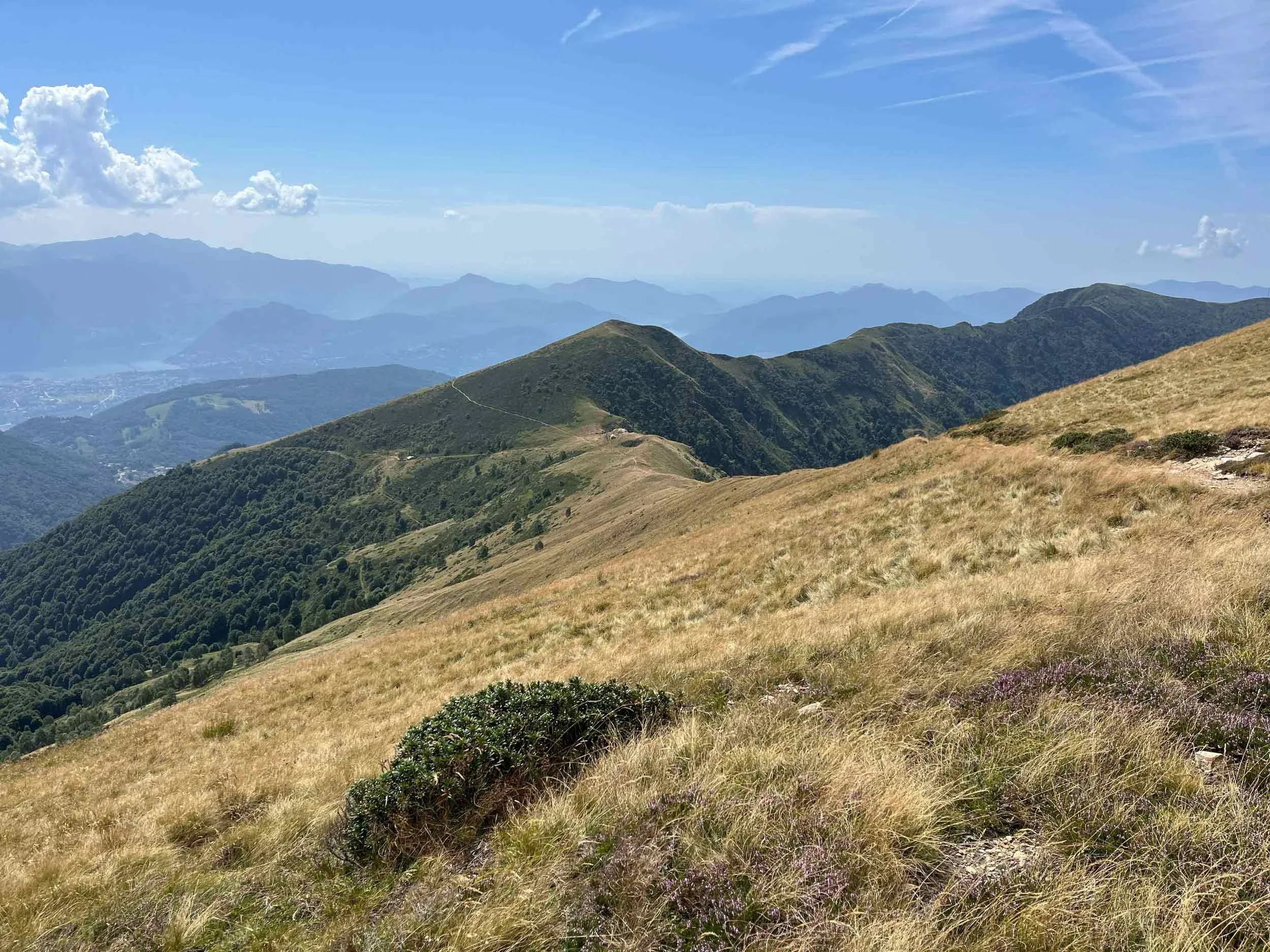 Blick auf grüne und braune Bergkuppen unter blauem Himmel mit Wolken und Fernblick auf weitere Bergketten.