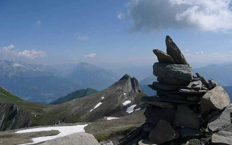 Berglandschaft mit Felsen, some Schneeflecken, im Hintergrund Berge und Himmel mit Wolken.