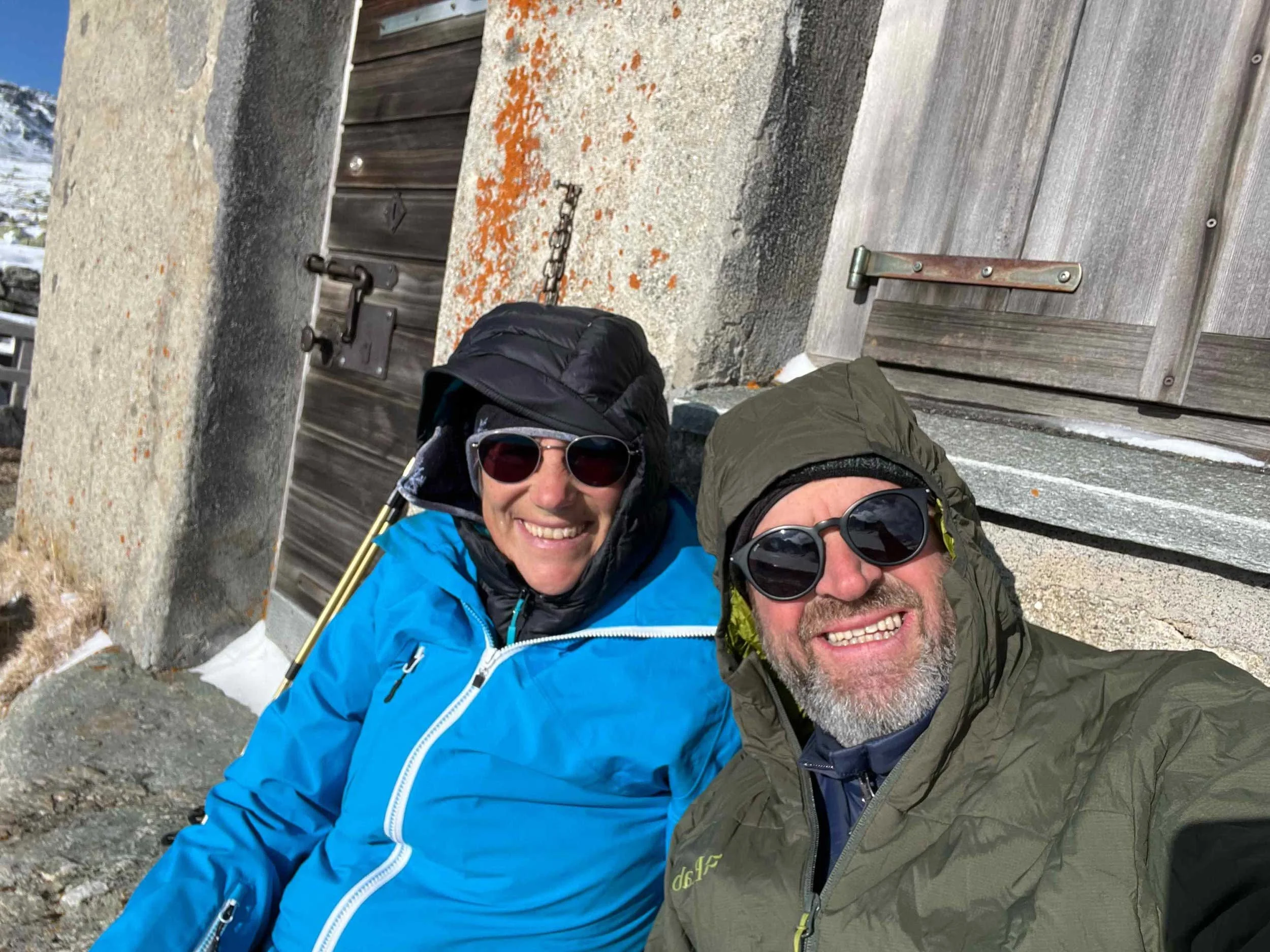 Zwei Menschen im Winteroutfit, die ein Foto auf einem bergigen Gebiet mit Holz- und Steinelementen machen.