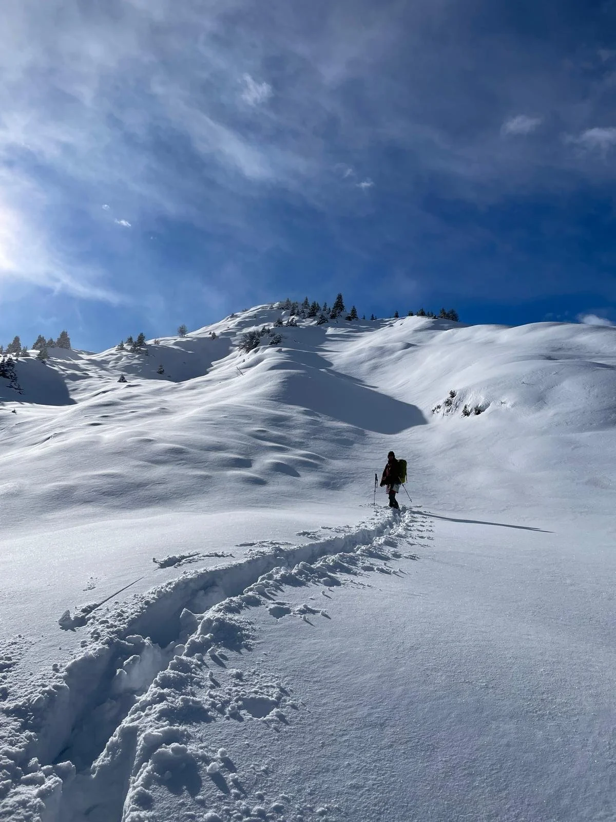 Ein einzelner Skitourengeher wandert durch tiefen Schnee in einem verschneiten Gebirge unter einem blauen Himmel mit wenigen Wolken.