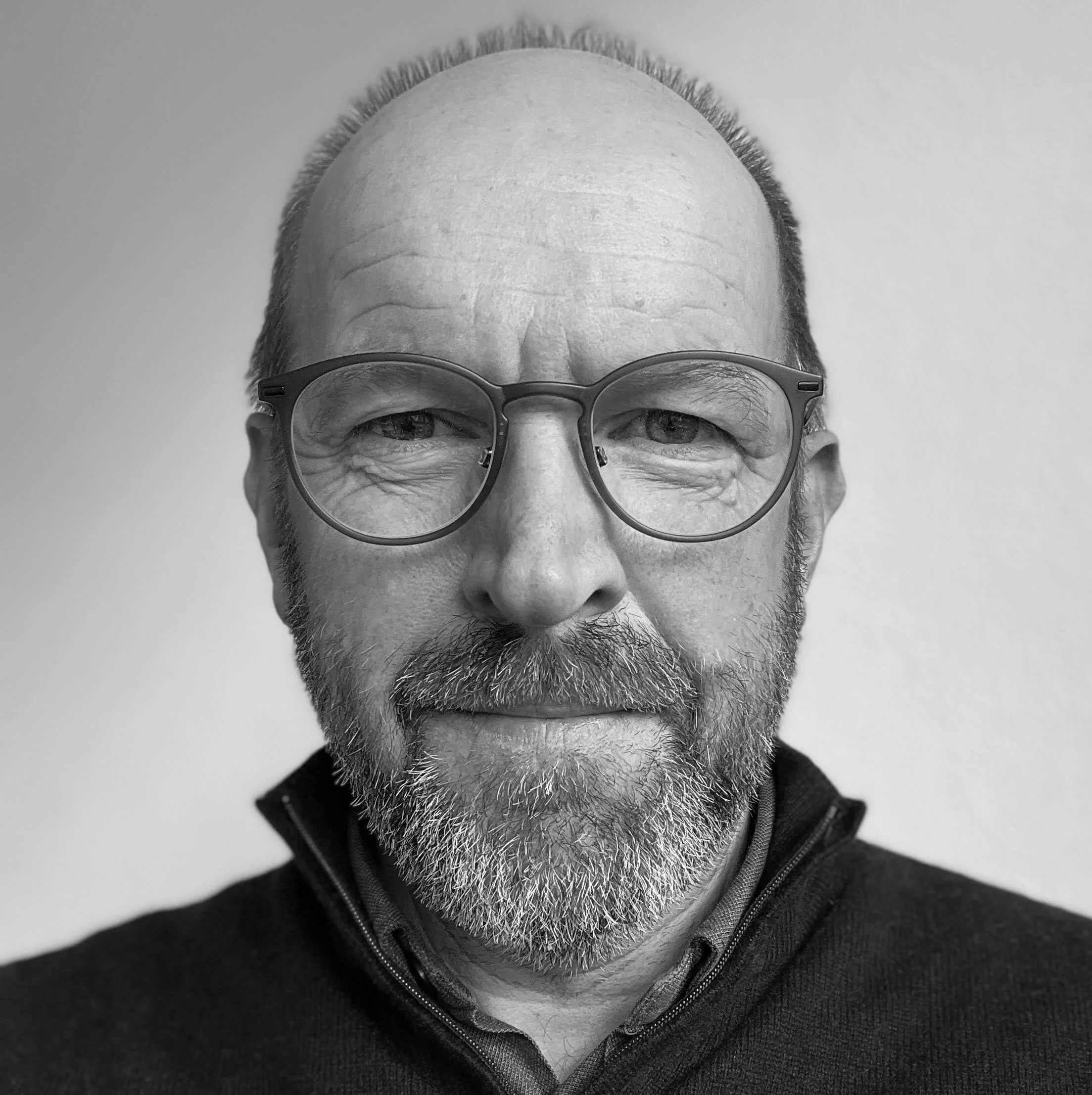 Schwarz-weiß-Porträt eines Mannes mit Brille und grauem Bart, zentriert, neutraler Hintergrund.