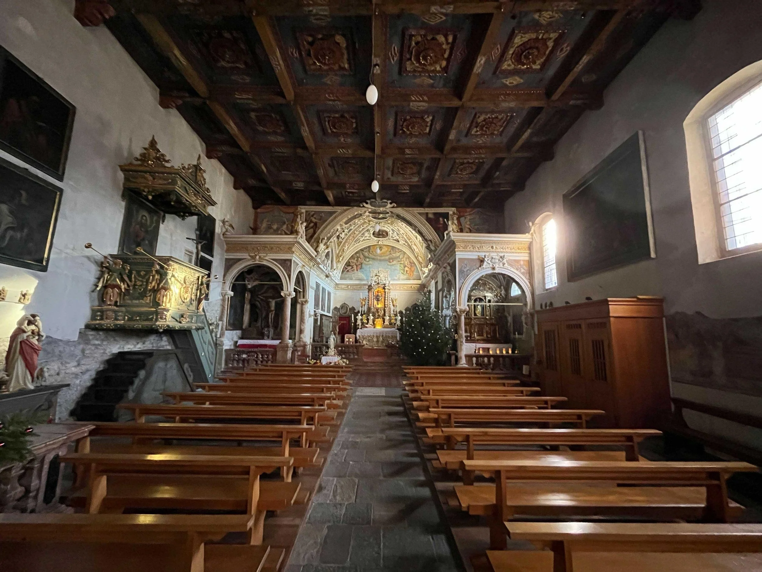 Innenraum einer Kirche mit hohen Bänken, einem Altar, einer Weihnachtsbaum und barockem Dekor an der Decke und Wänden.