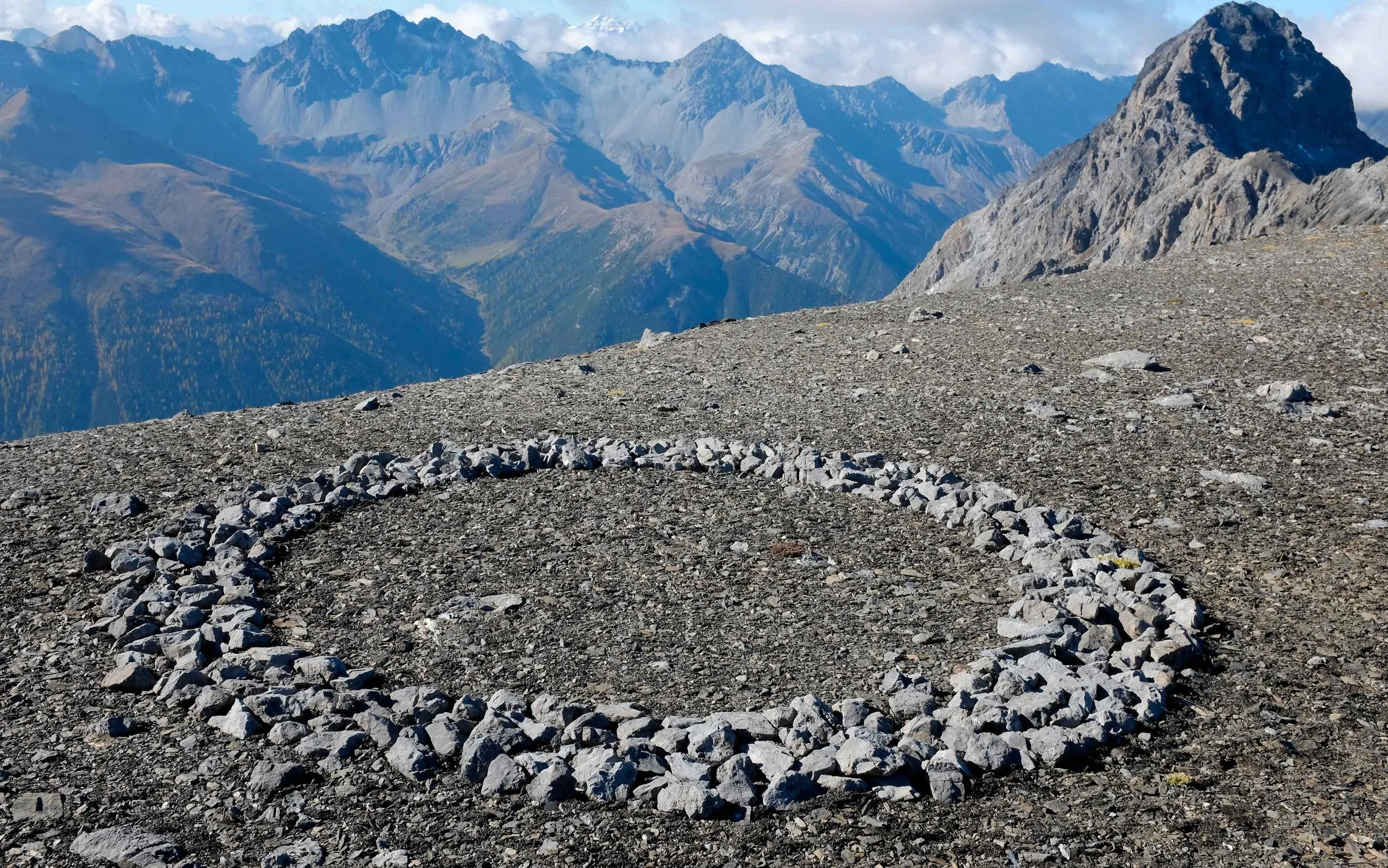In den Bergen liegt auf dem felsigen Boden eine größere ovale Markierung aus Steinen.
