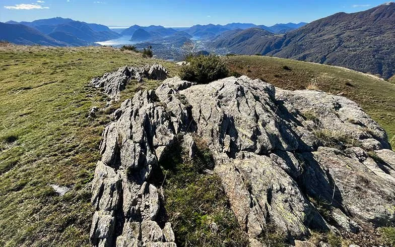 Berglandschaft mit Felsen, grünen Hügeln und einer Stadt im Tal, umgeben von Bergen unter klarem Himmel.