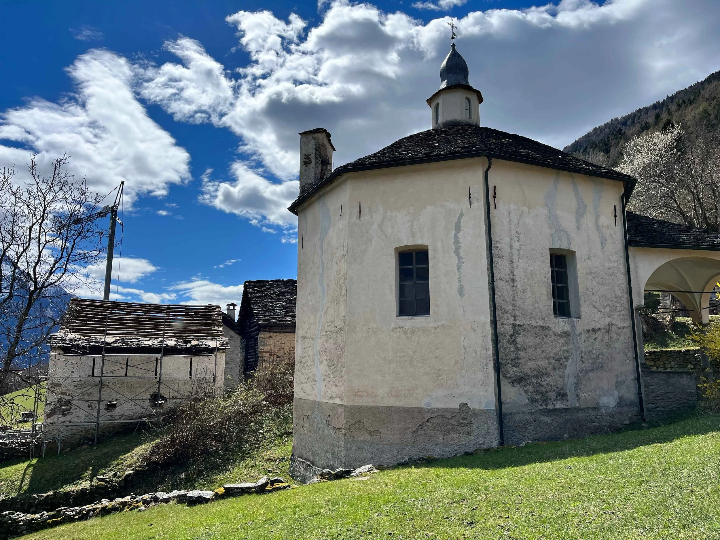 Alte Kirche mit hellgelber Wand und dunklem Dach, umgeben von grünem Rasen, mit blauen Himmel und Wolken im Hintergrund.