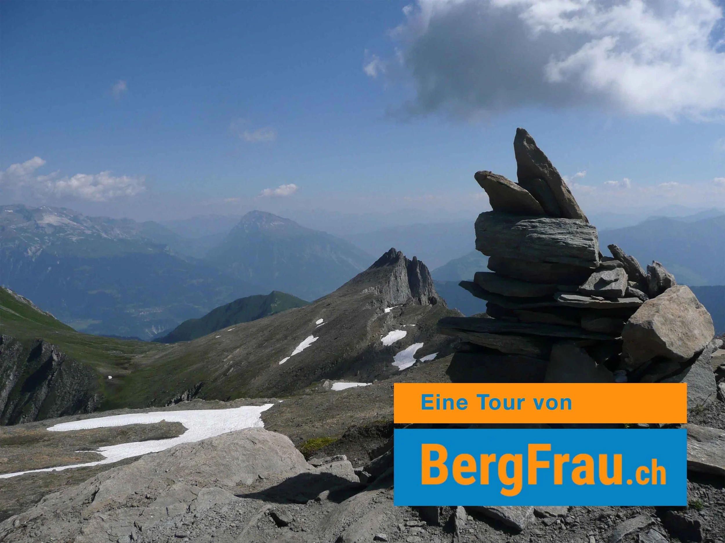 Berglandschaft mit Felsformation im Vordergrund und mehreren Bergen im Hintergrund, einige Schneefelder auf den Hängen, leicht bewölkter Himmel.