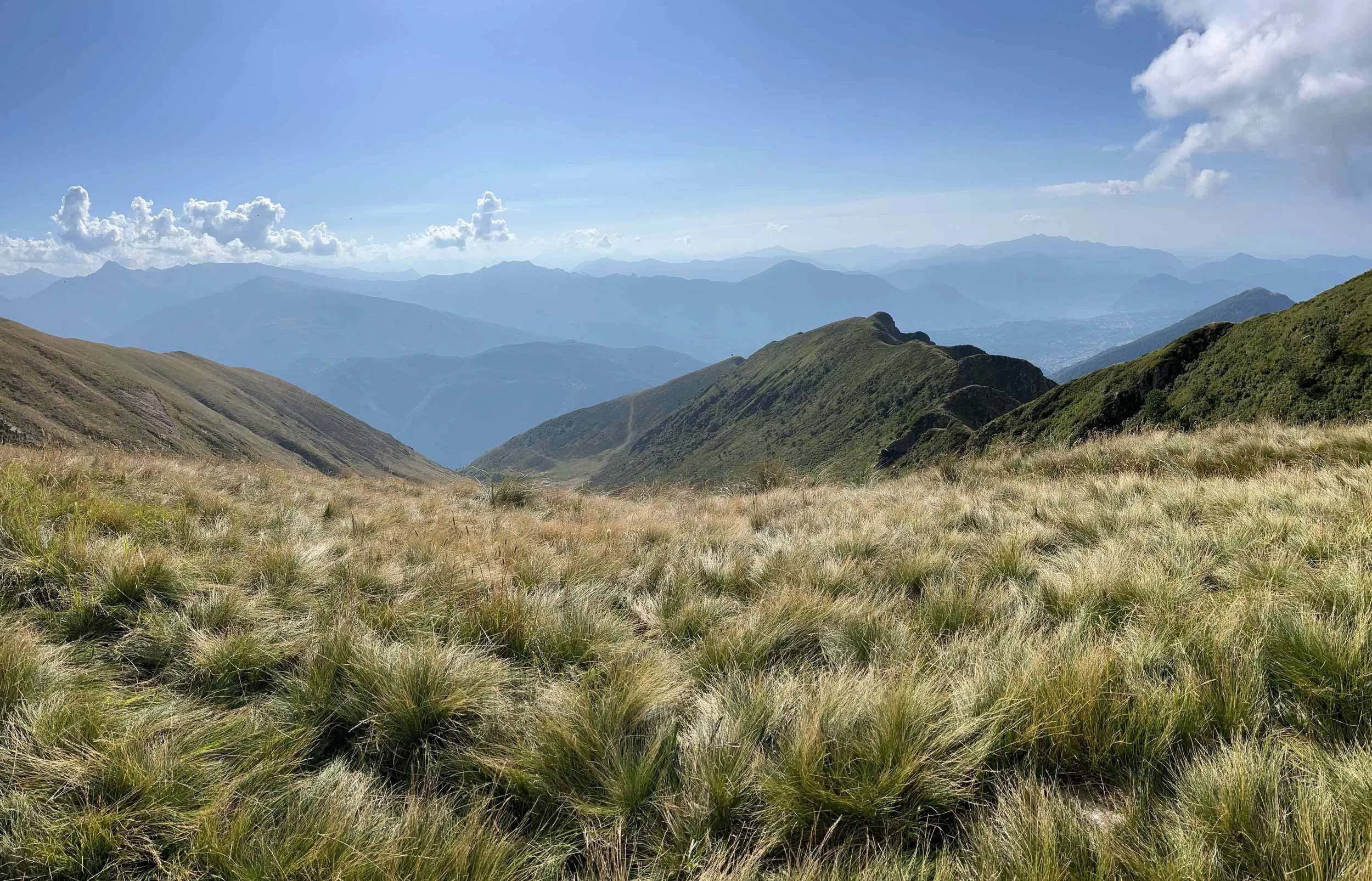 Berglandschaft mit grünen Hügeln, fernen Bergketten und blauen Himmel mit Wolken.