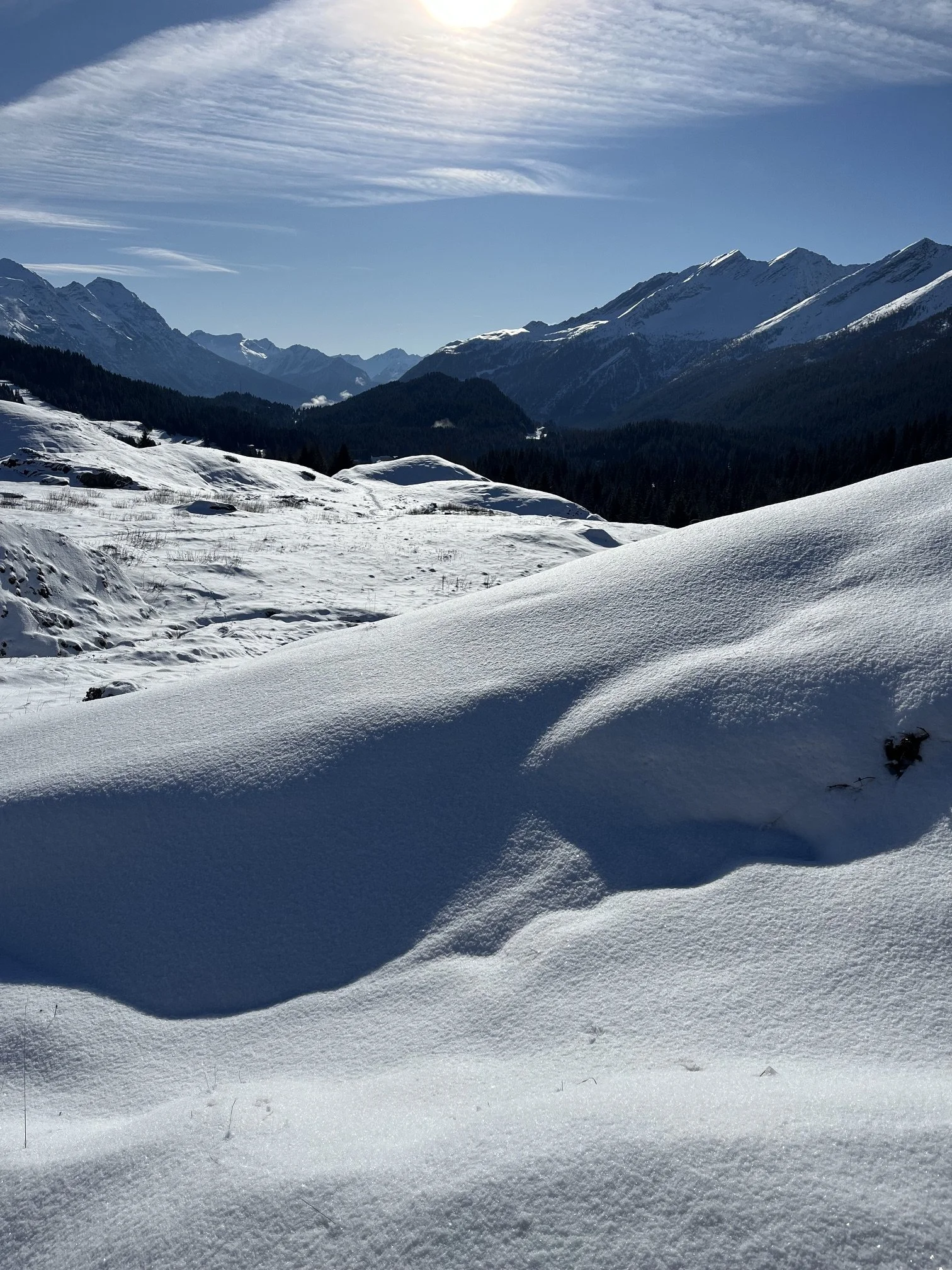 Schneebedecktes Tal mit Bergen im Hintergrund, blauer Himmel und Wolken
