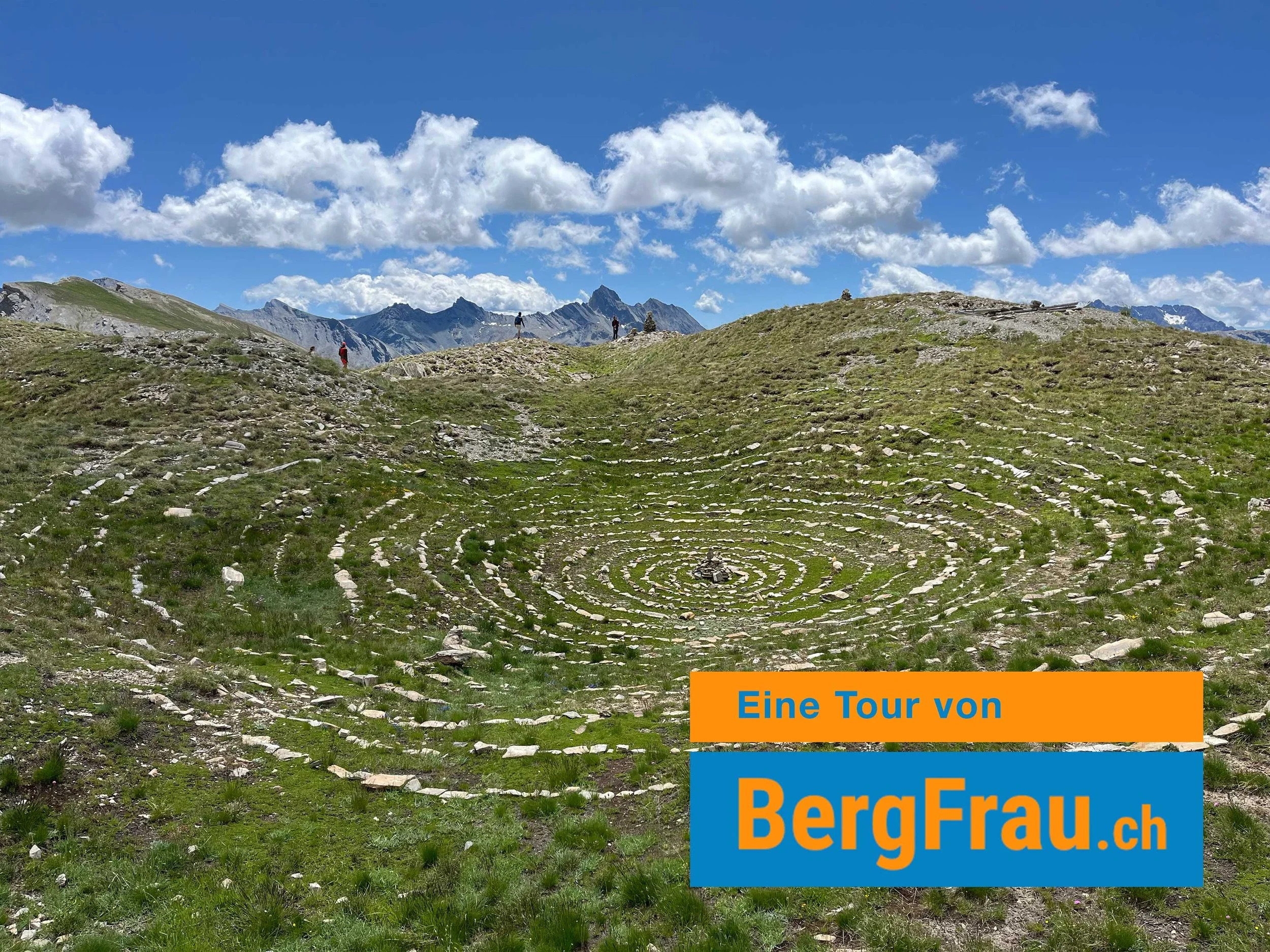 Ein grünes, wellenförmiges Tal mit kreisförmigen Mustern und Bergen im Hintergrund bei sonnigem Himmel.