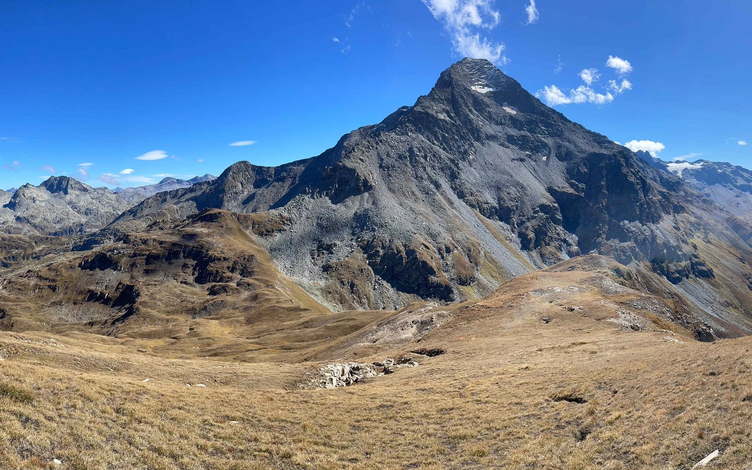Berglandschaft mit großem, schroffen Gipfel, trockenen Wiesen im Vordergrund und klarem blauen Himmel