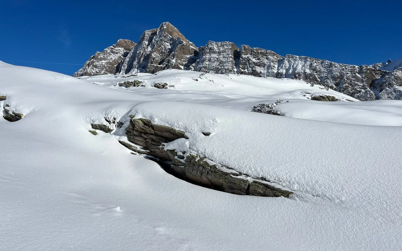 Schneebedeckte Berge und Schnee im Vordergrund mit vereinzelten Steinen
