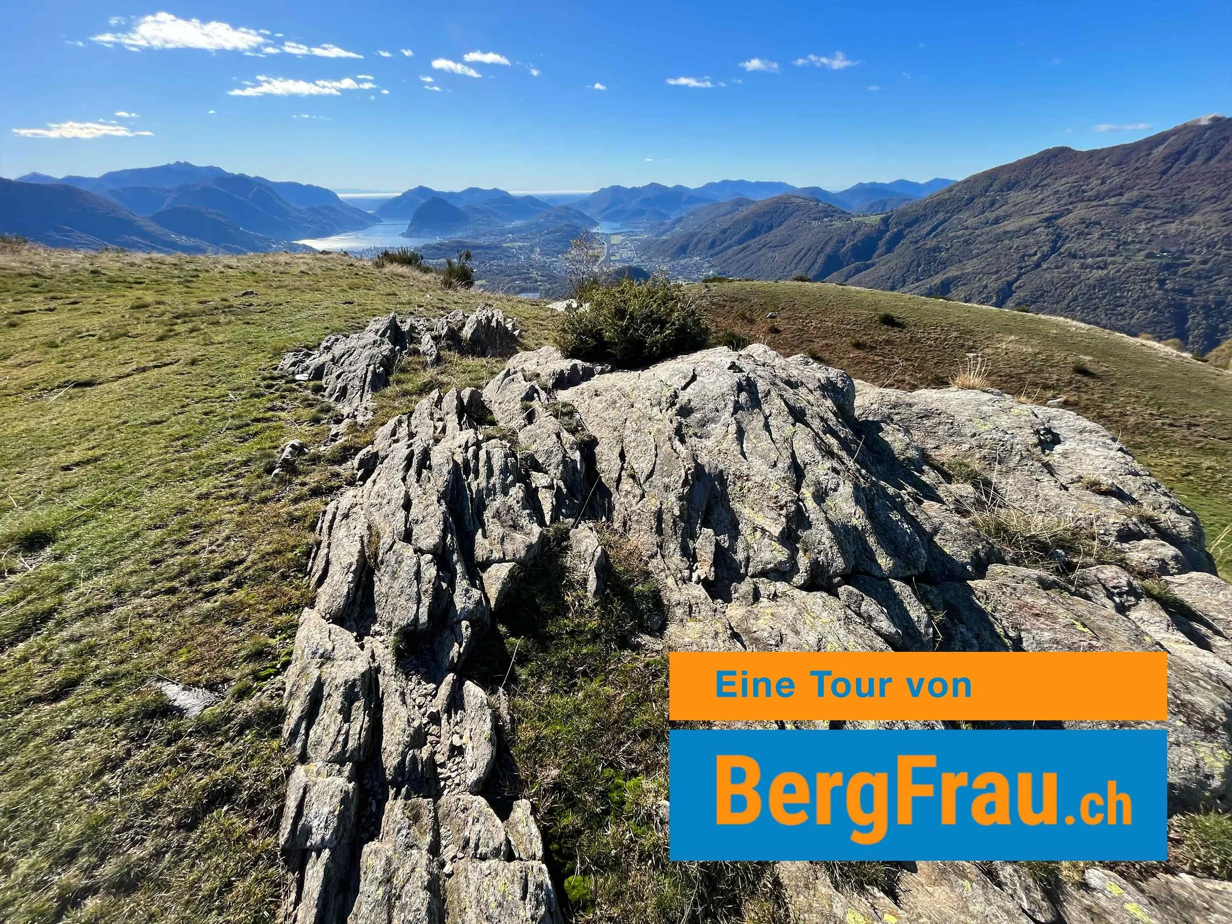 Berglandschaft mit Felsen, grünen Hängen, Bergen im Hintergrund und blauer Himmel mit Wolken, Werbung für eine Bergtour auf BergFrau.ch